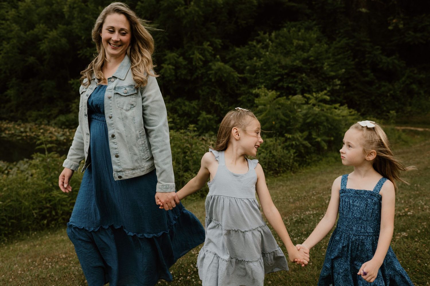 A family walks hand-in-hand through a green field wearing coordinating blue and gray outfits.