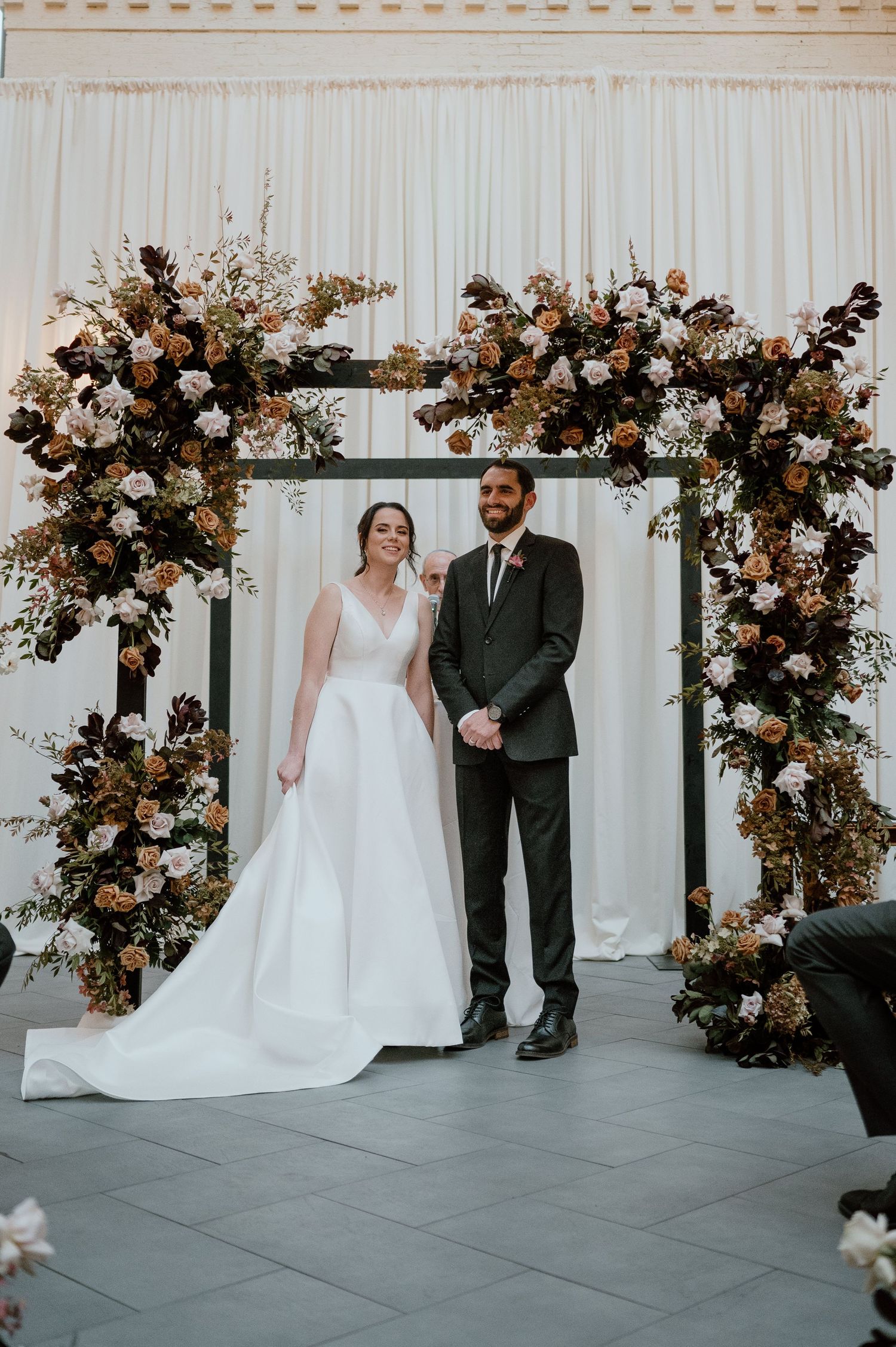 Elegant wedding ceremony setup with dramatic floral arch and white backdrop.