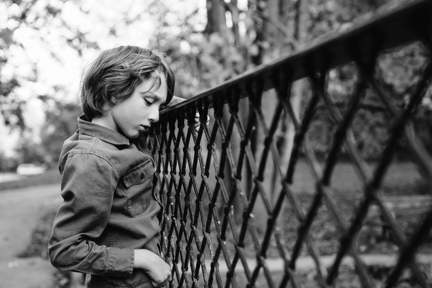 Black and white portrait of someone looking through an ornate metal fence pattern.