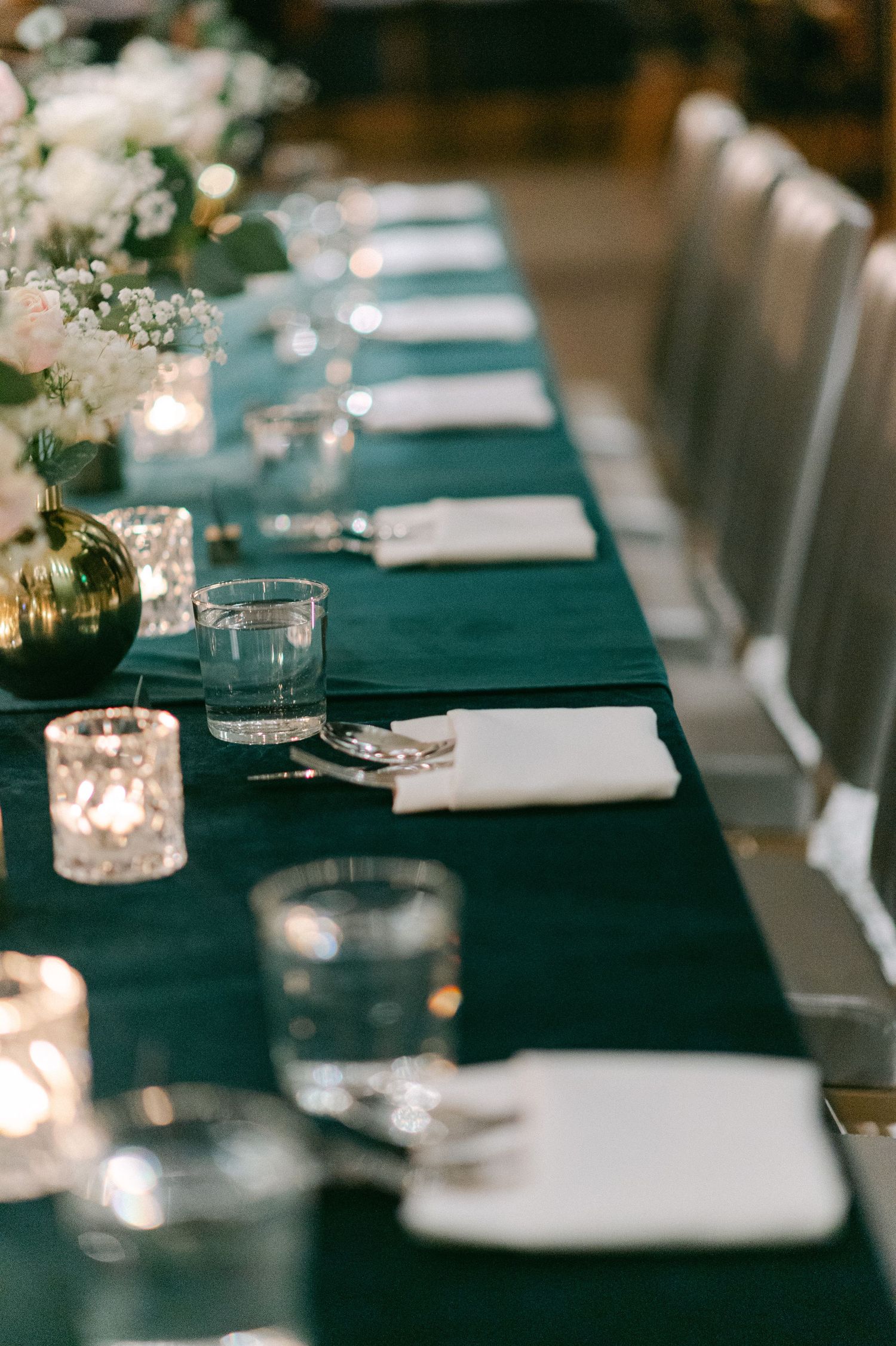 Formal table setting with emerald tablecloth, white napkins and glowing candle votives.