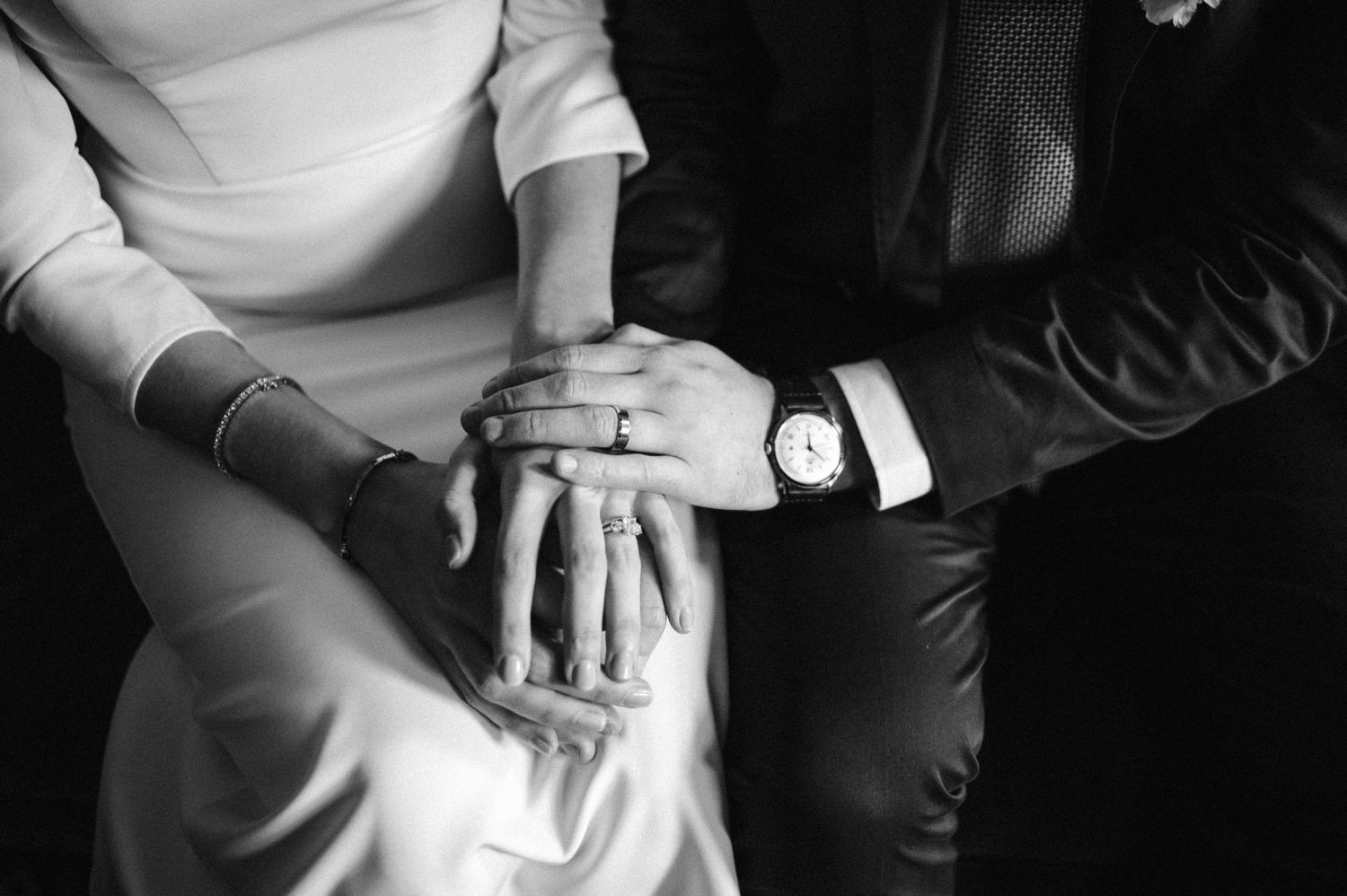 Close-up black and white photo of hands with rings resting together on formal attire.