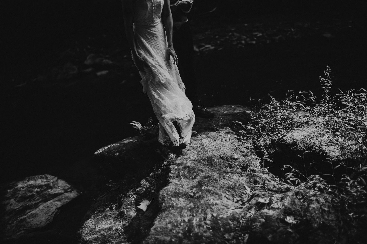 Close-up black and white shot of feet stepping on mossy rocks.