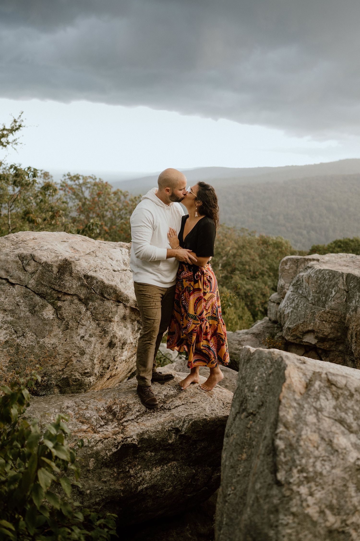 Romantic couple sharing an intimate moment on rocky mountain overlook at sunset.