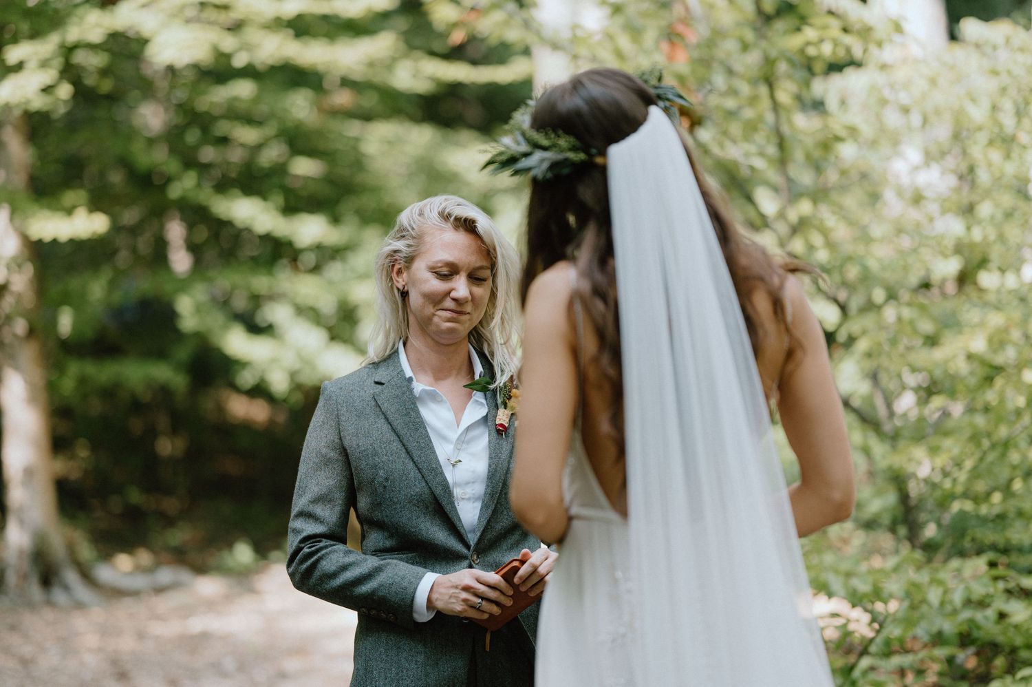 A tender moment between a couple in wedding attire amid a green forest setting.