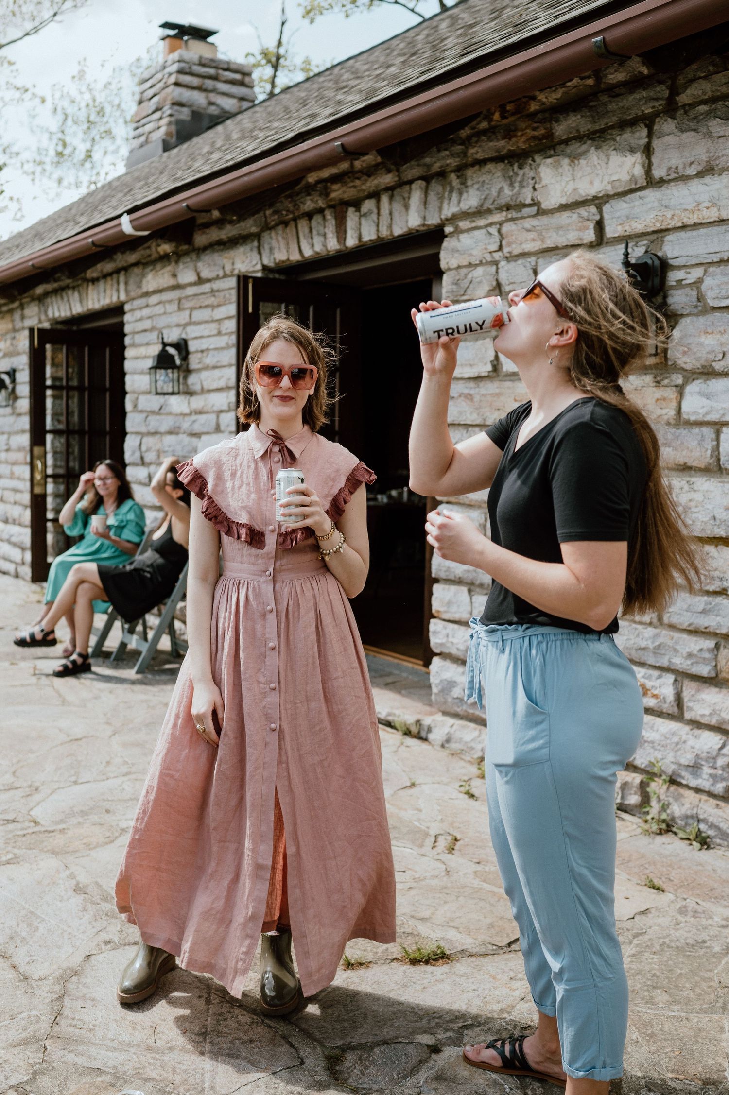 People enjoying drinks outside a rustic stone building on a sunny day.