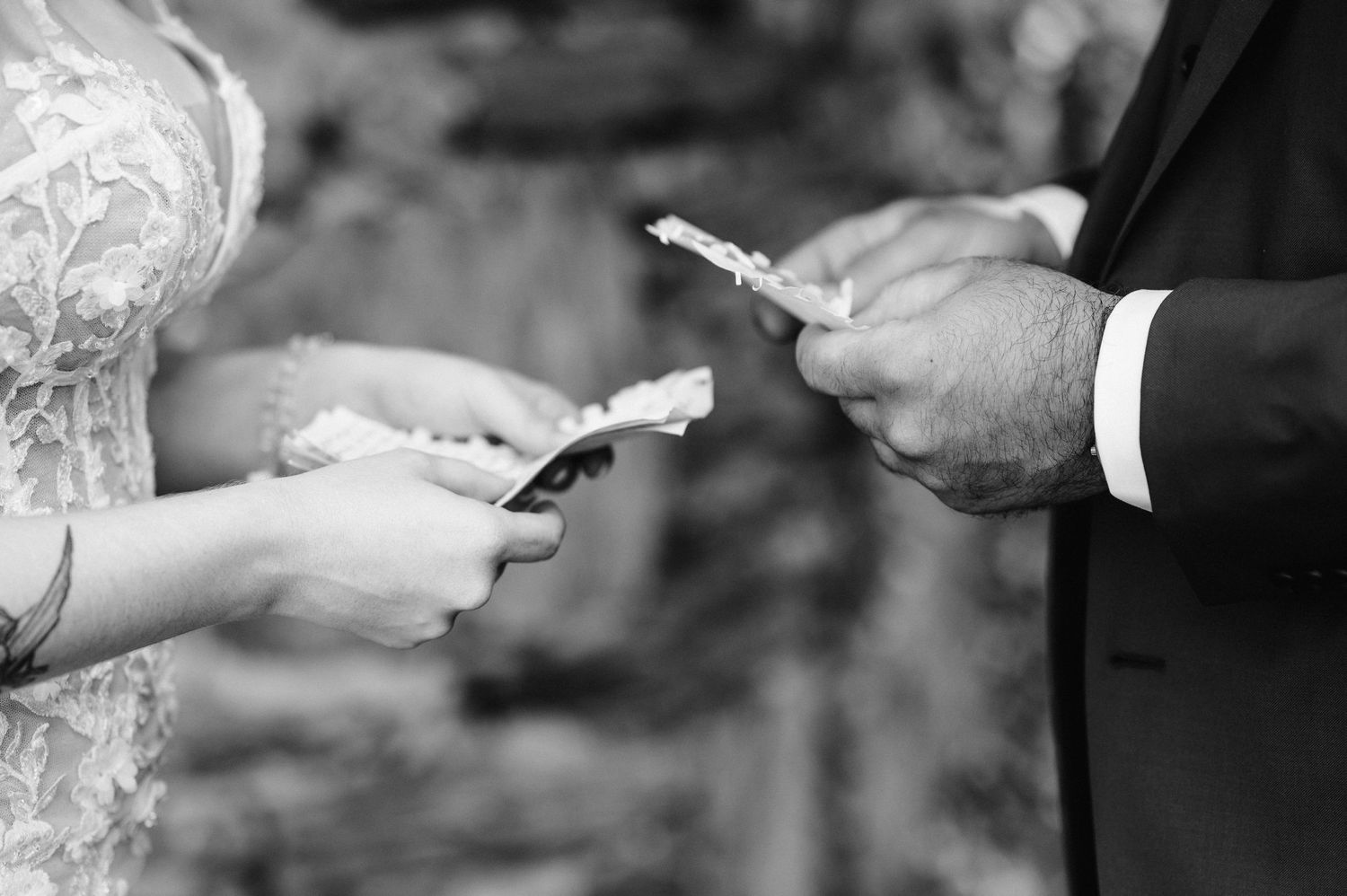 Black and white close-up of hands exchanging rings during a wedding ceremony.