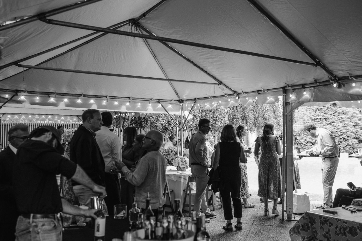 Wedding guests mingling under tent at outdoor reception in black and white.