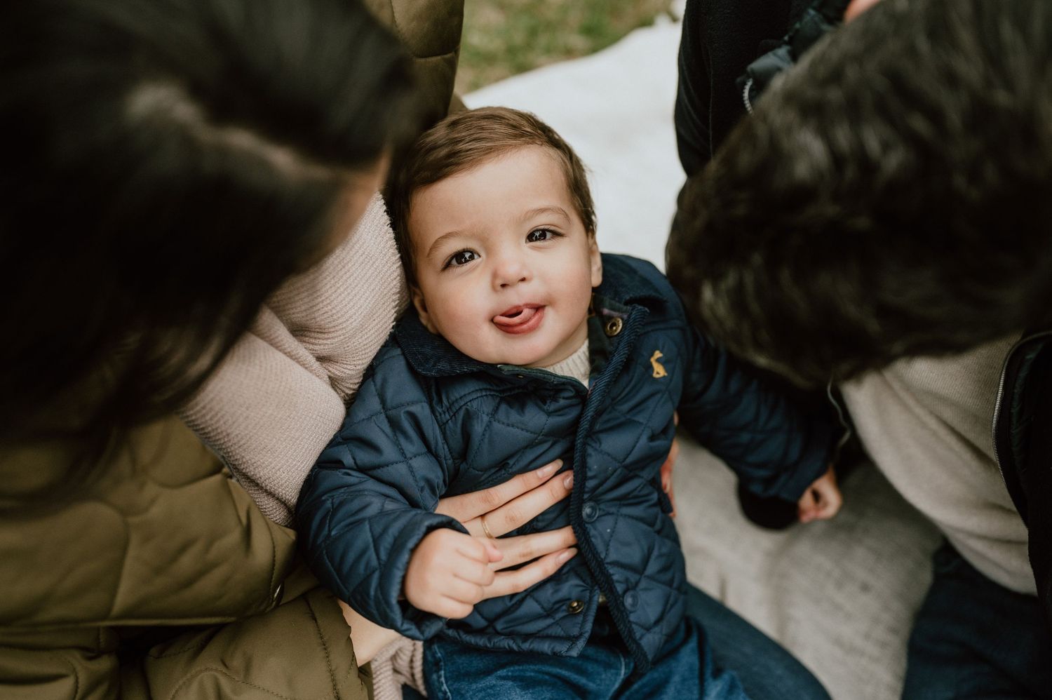 Close up shot of laughing toddler in blue jacket surrounded by adults.
