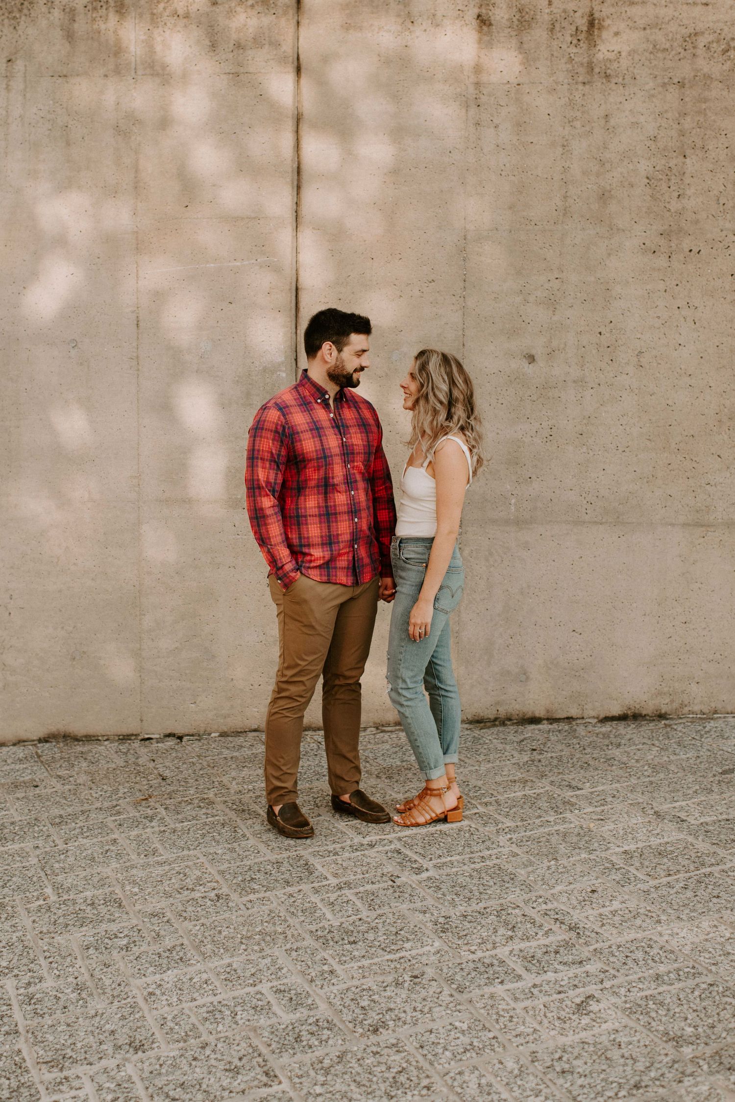 Couple in casual attire standing against concrete wall with red plaid shirt and denim.