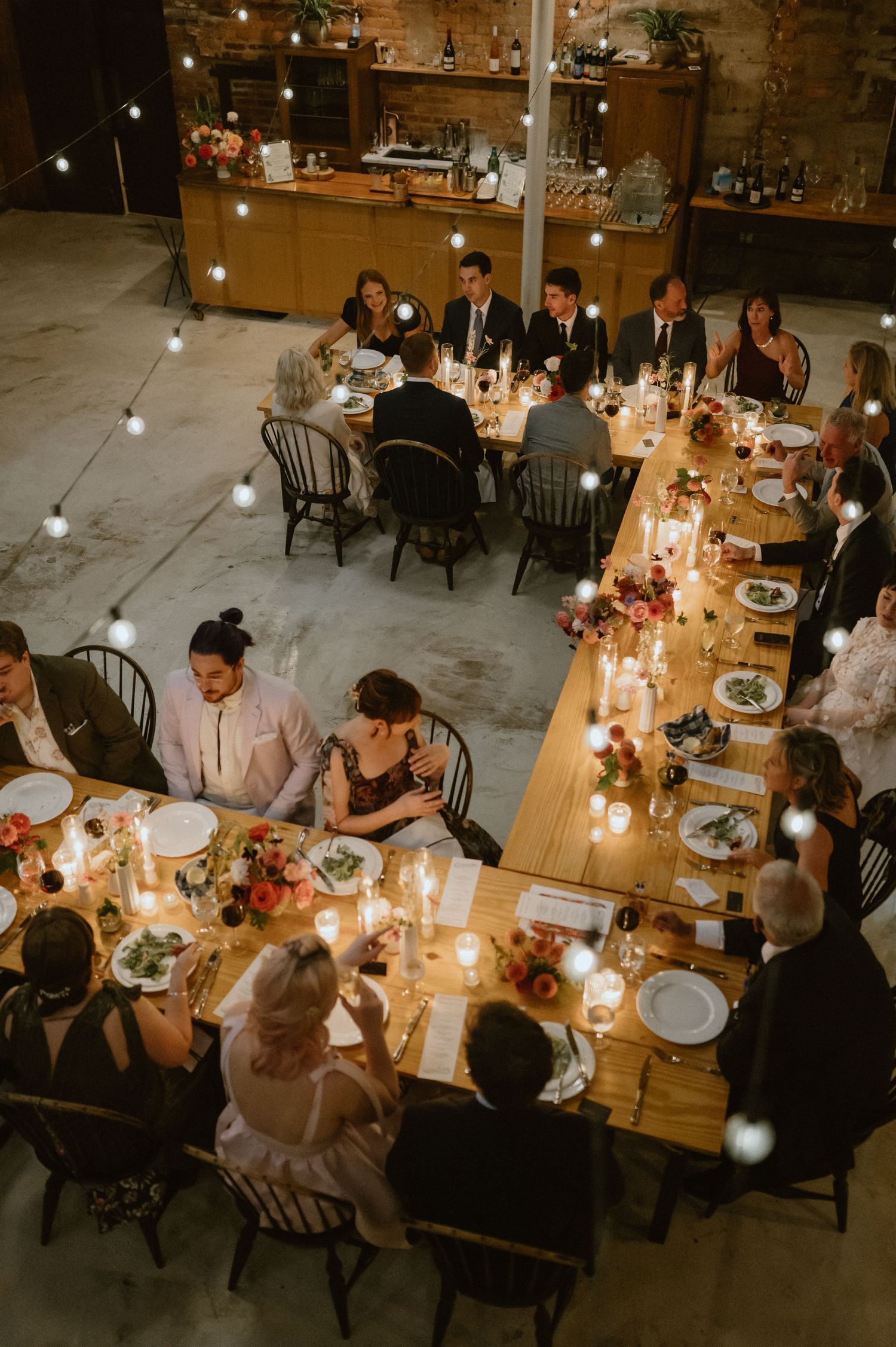 Overhead view of wedding reception dinner with guests seated at long wooden tables with candlelight.