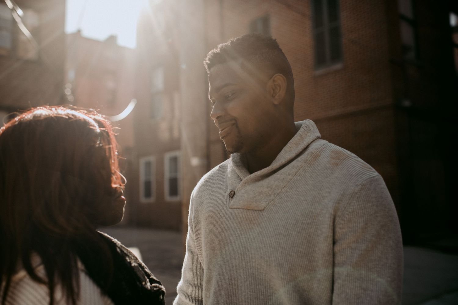 A couple shares a candid moment in warm sunlight against an urban backdrop.