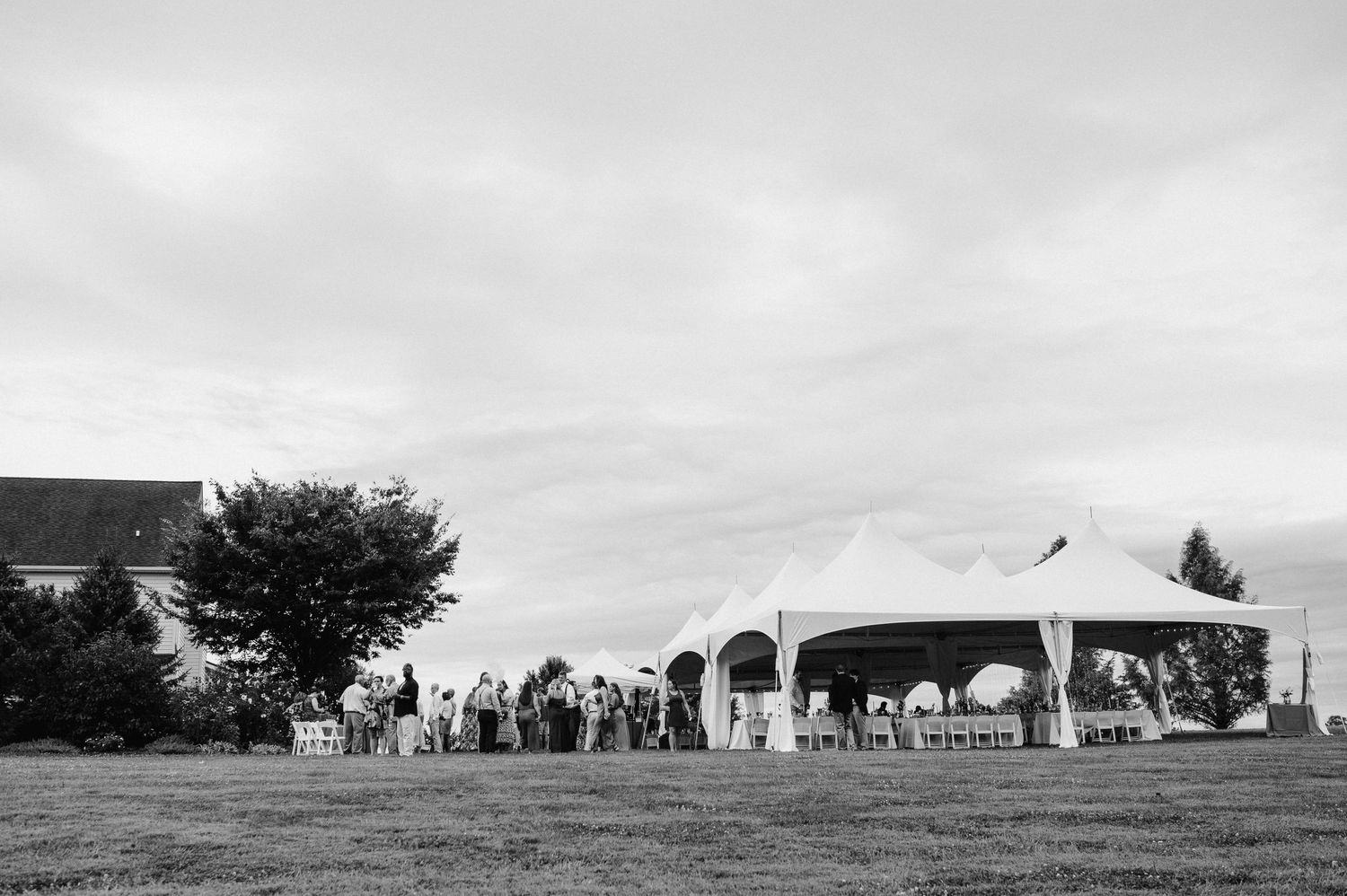 A black and white photo of a wedding reception setup with tents and guests on a grassy lawn.