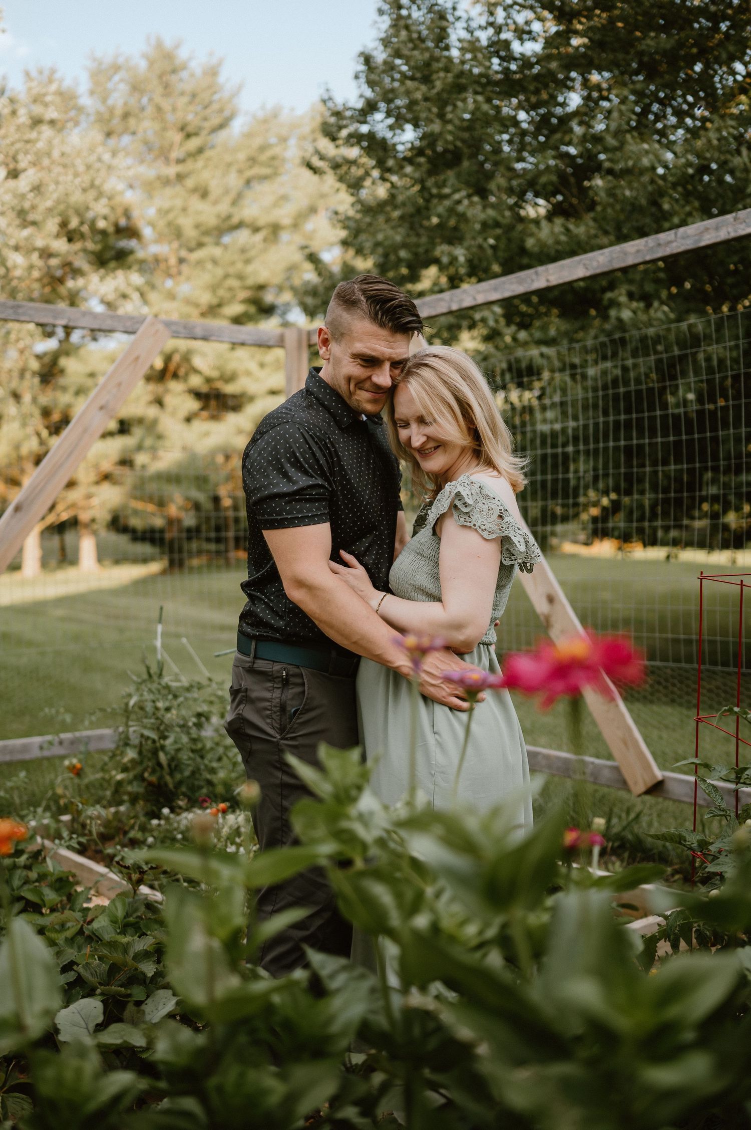 A tender embrace in a backyard garden with red flowers and a wire fence in the background.