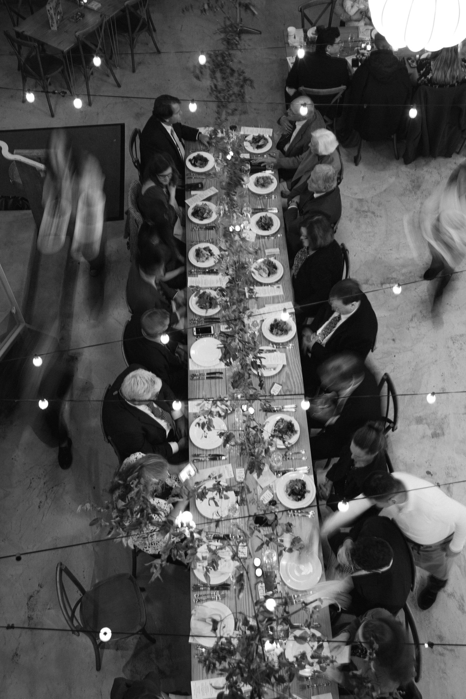 Overhead view of an elegant wedding reception dinner table with string lights and place settings.