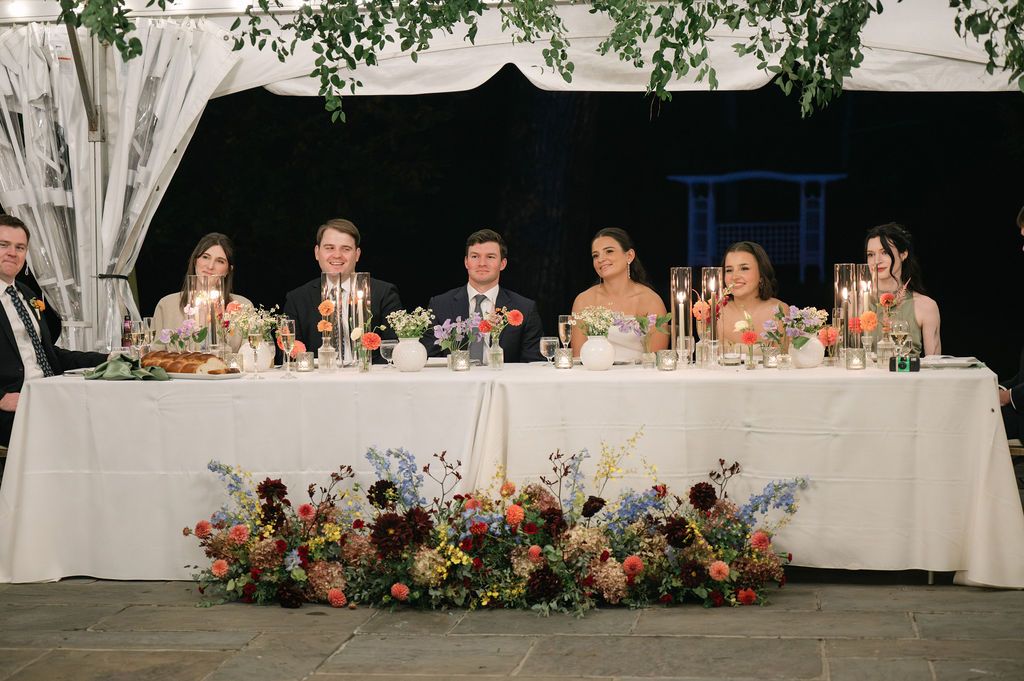 Long wedding reception head table decorated with floral arrangements and white linens at Strong Mansion on Sugarloaf Mountain