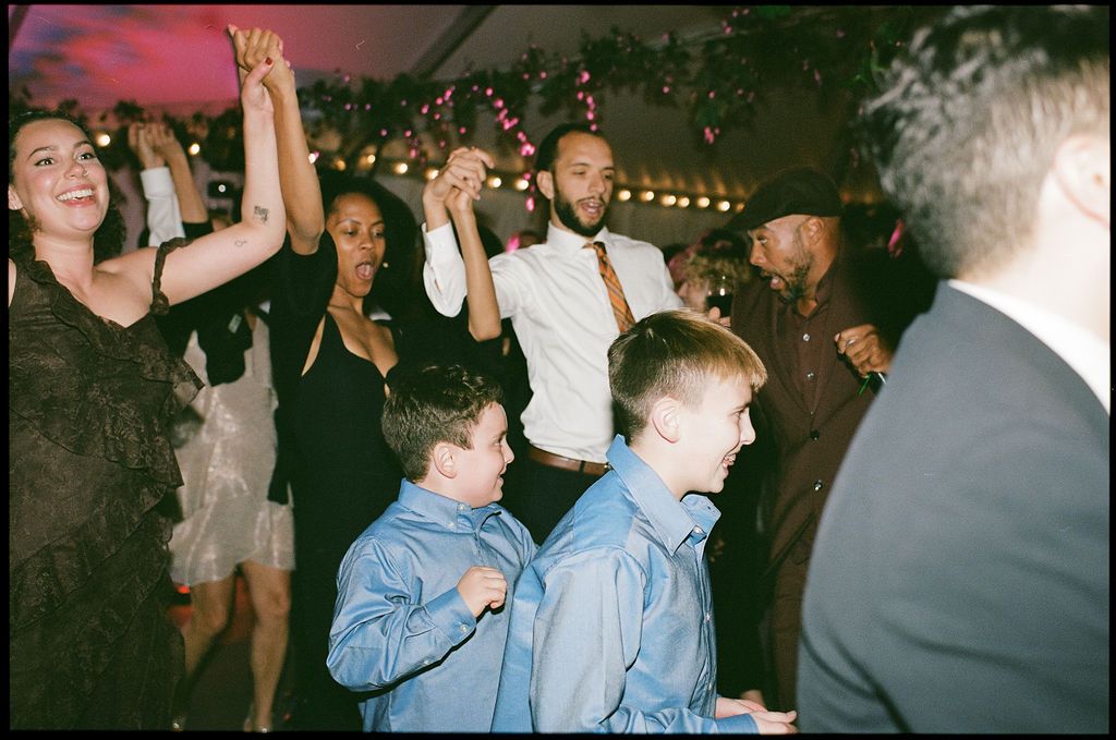 Wedding guests and children dance together at an evening reception celebration.