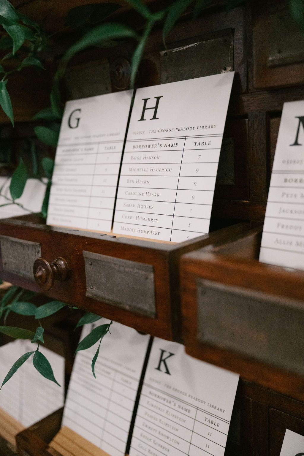 Wedding seating cards displayed on wooden church pews with green foliage accents at George Peabody Library Wedding in Baltimore