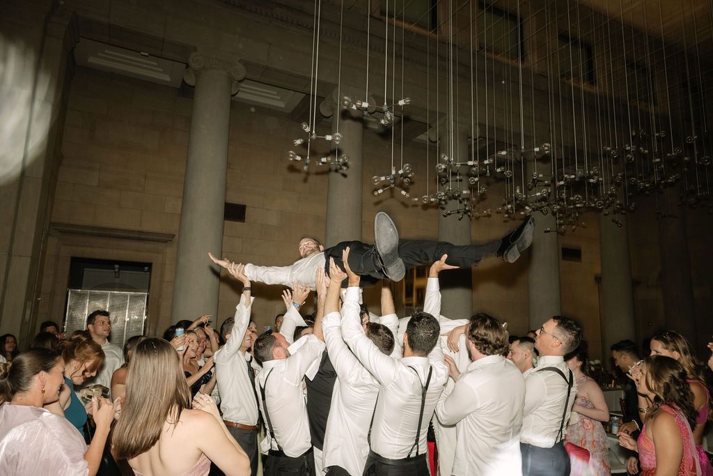 Wedding reception guests dance and celebrate with raised arms on a crowded dance floor in an elegant venue.