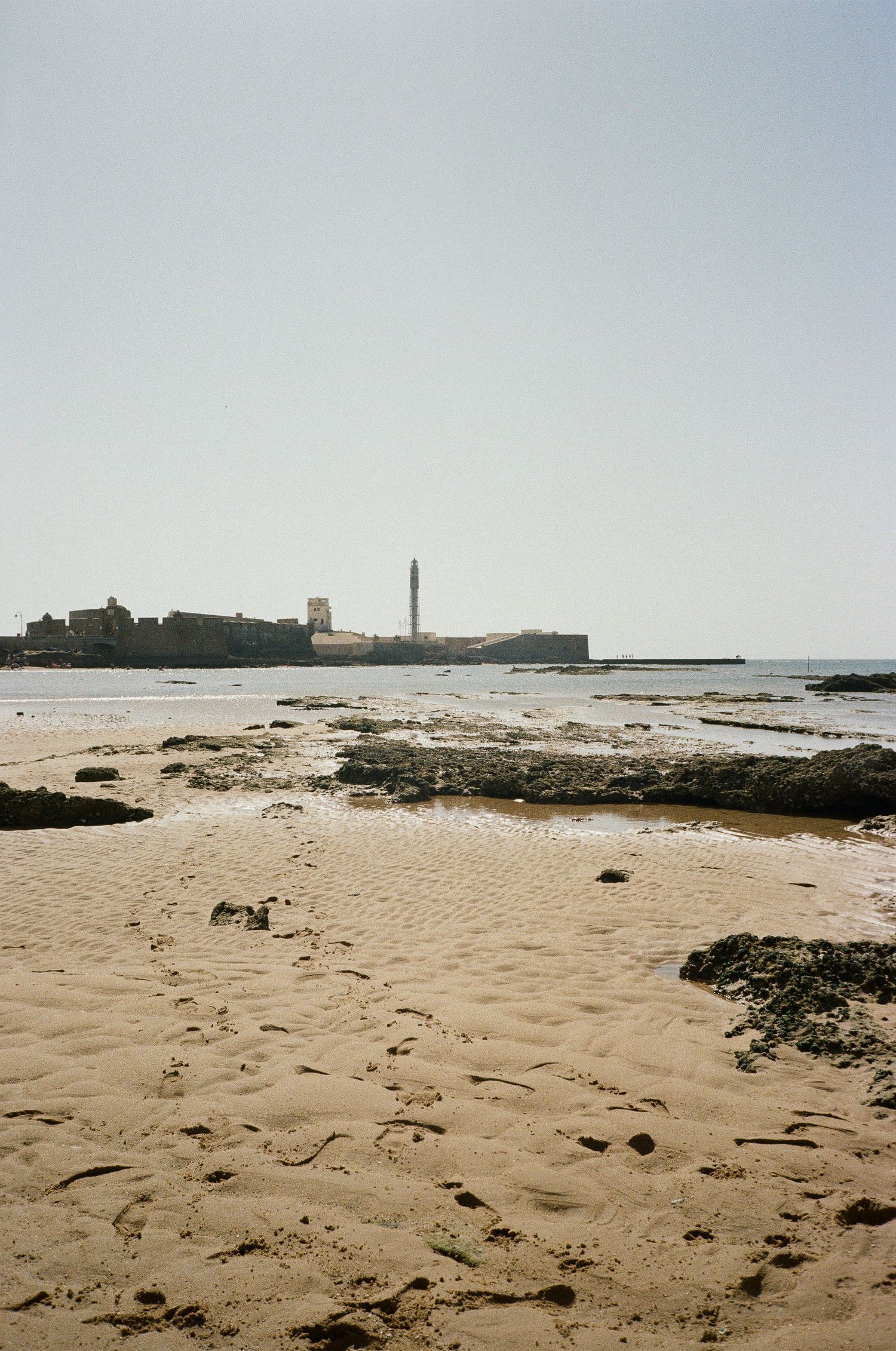 Lighthouse and coastal buildings viewed from a rocky beach during low tide.