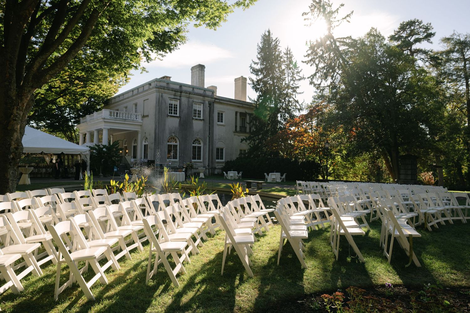 White folding chairs set up for an outdoor wedding ceremony with trees casting long shadows.