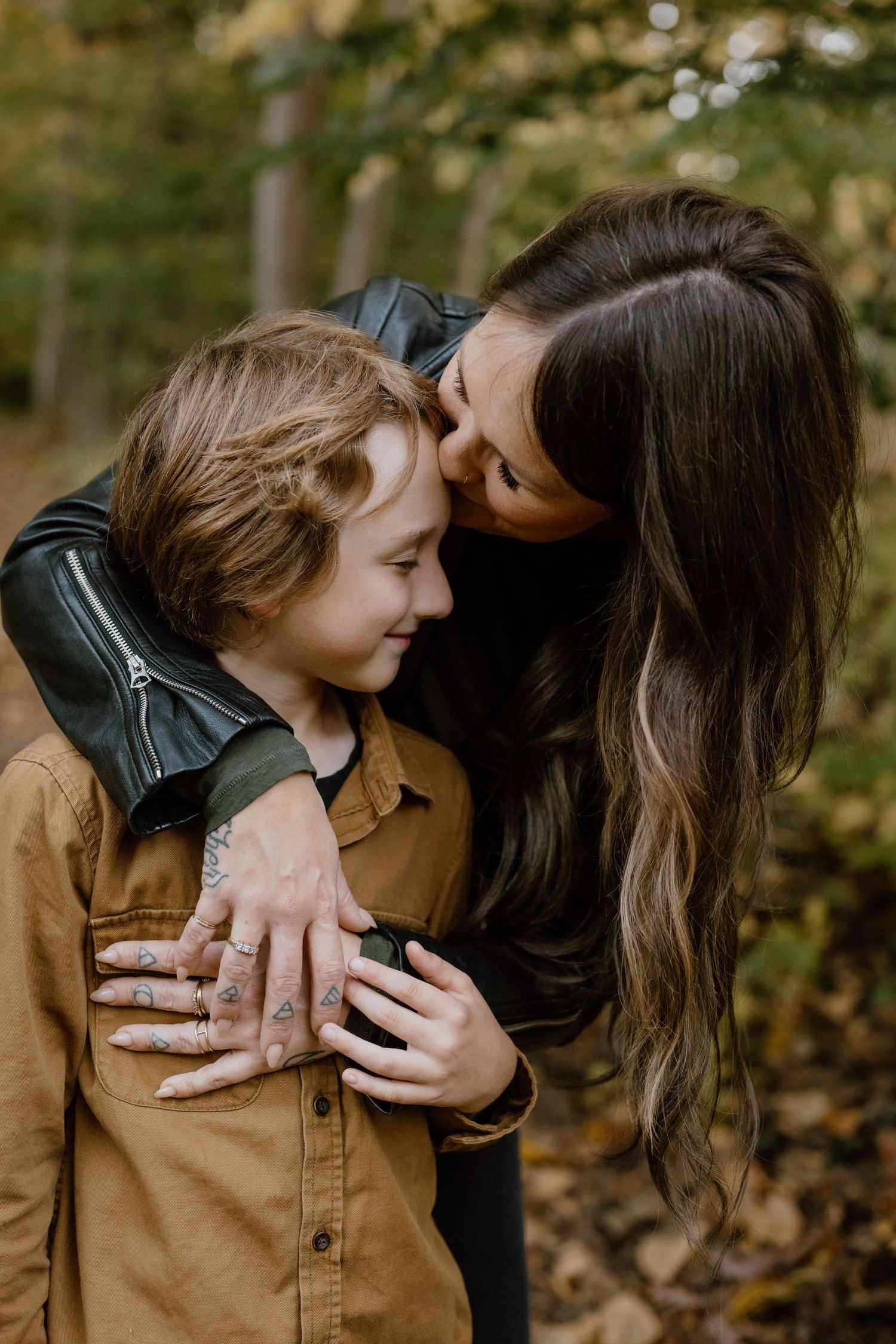 A tender embrace between two people wearing contrasting jackets against a backdrop of fall foliage.