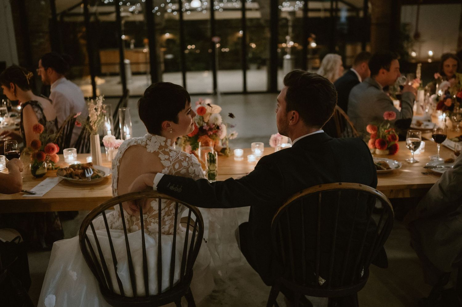 Intimate wedding reception dinner scene with couples seated at rustic wooden tables.