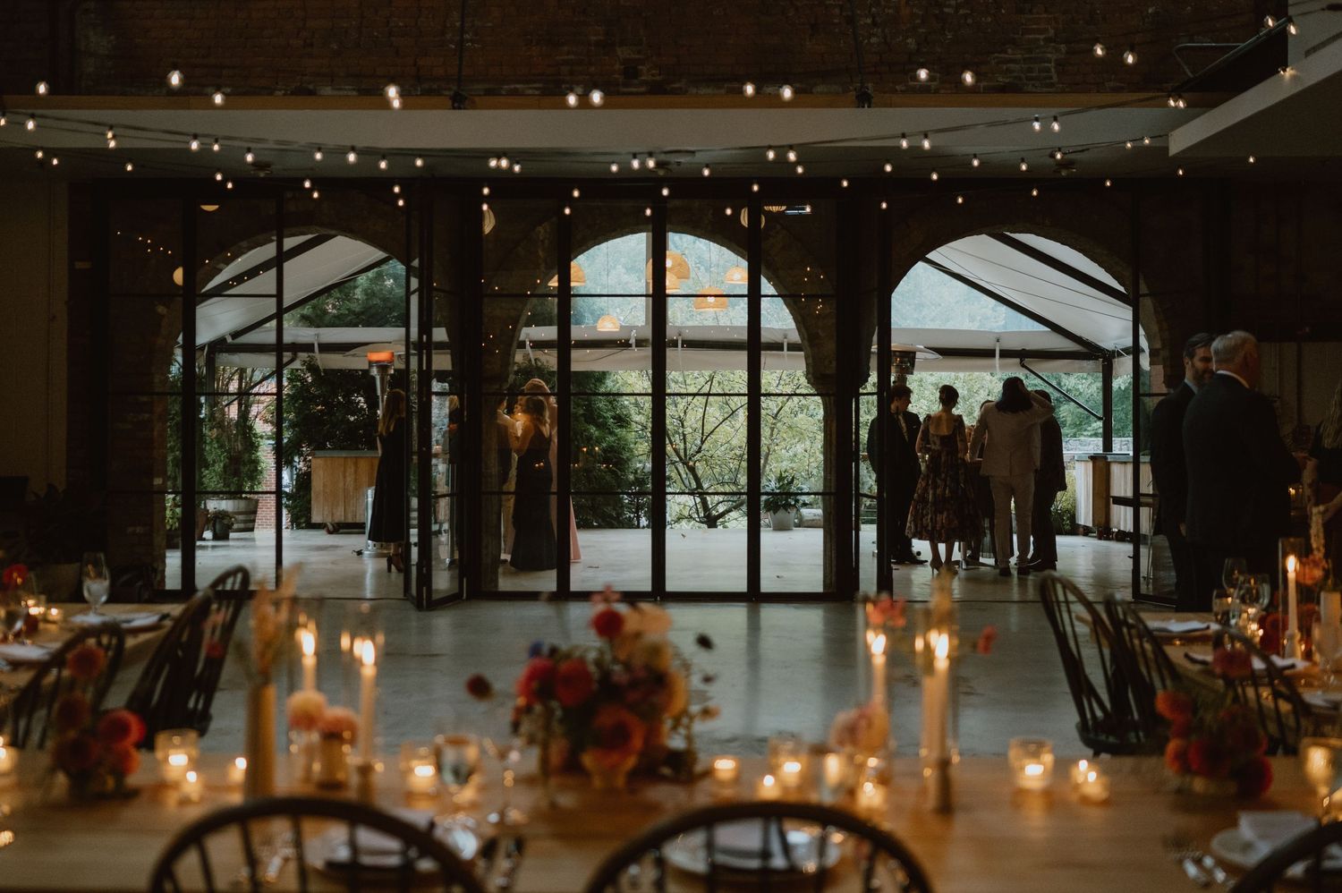 Reception venue with arched windows, string lights and candlelit tables creating a romantic atmosphere.