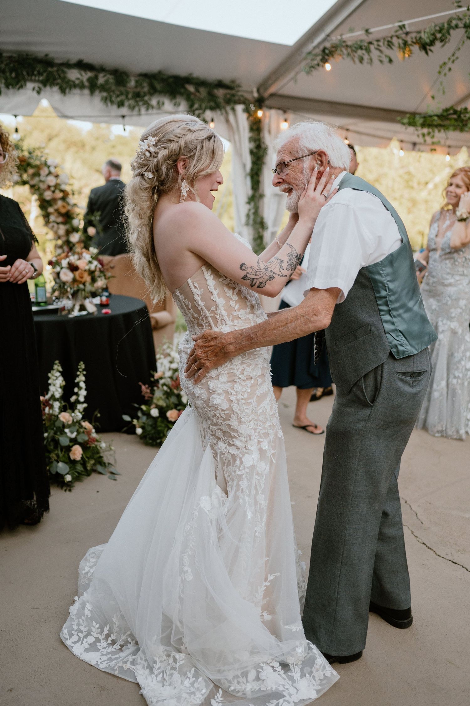 A tender dance moment between newlyweds under a decorated tent with floral arrangements.