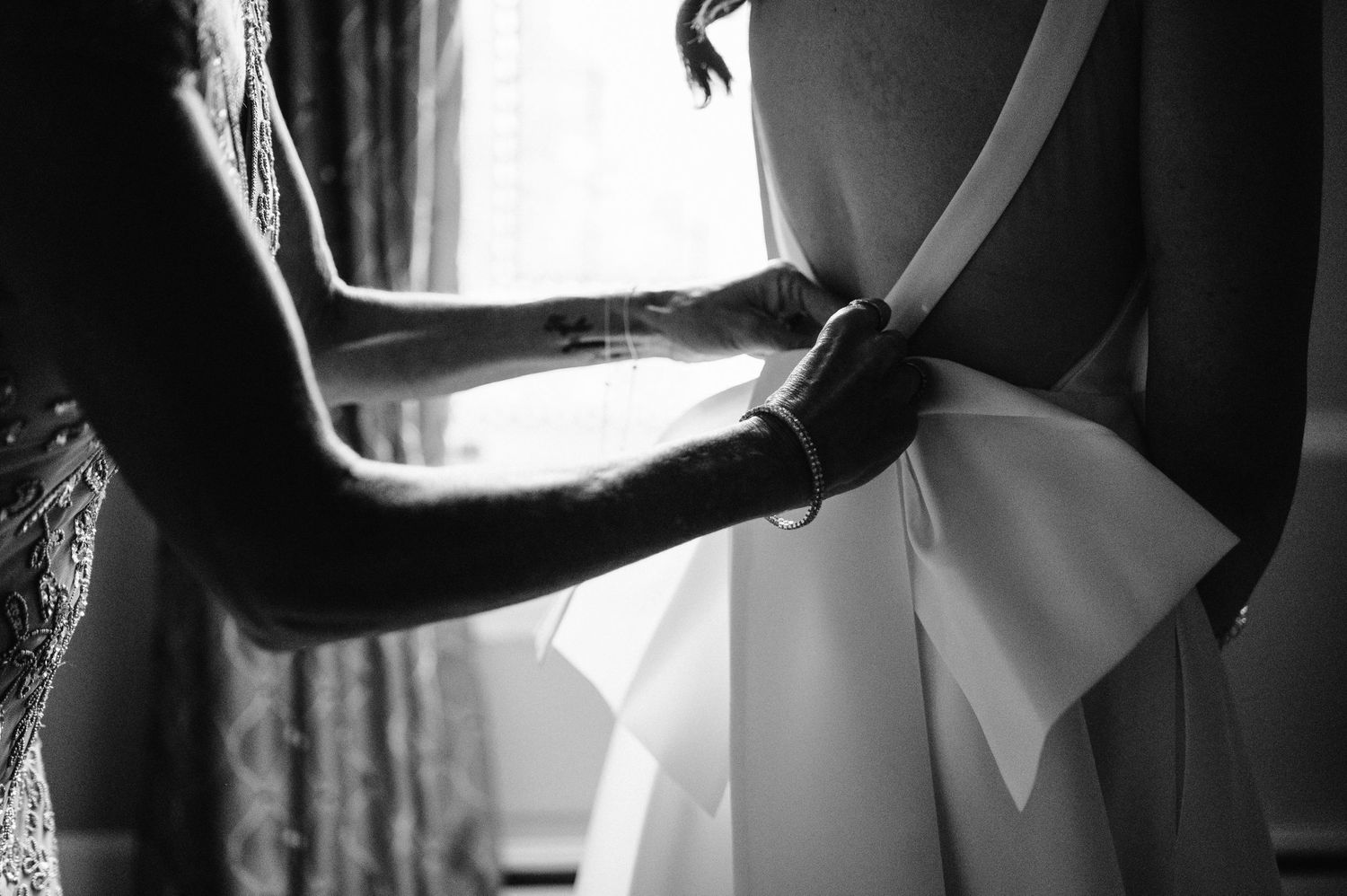 Black and white image showing hands adjusting the back of an elegant wedding dress.