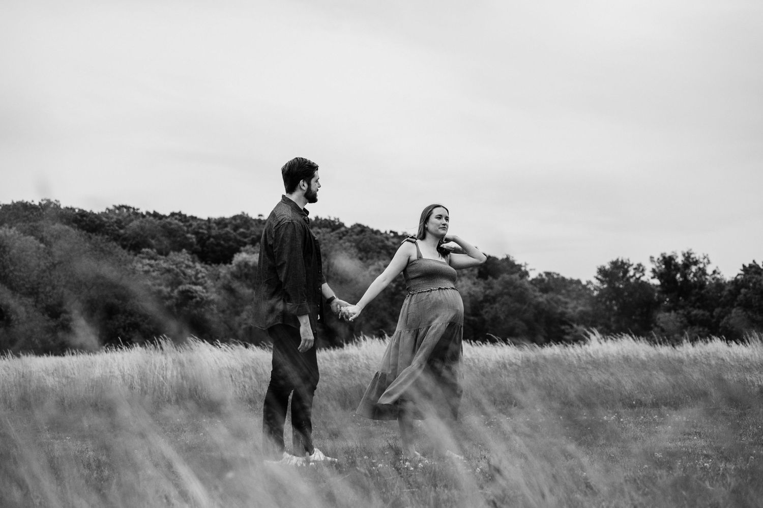 A playful black and white photo of a couple dancing in a field.
