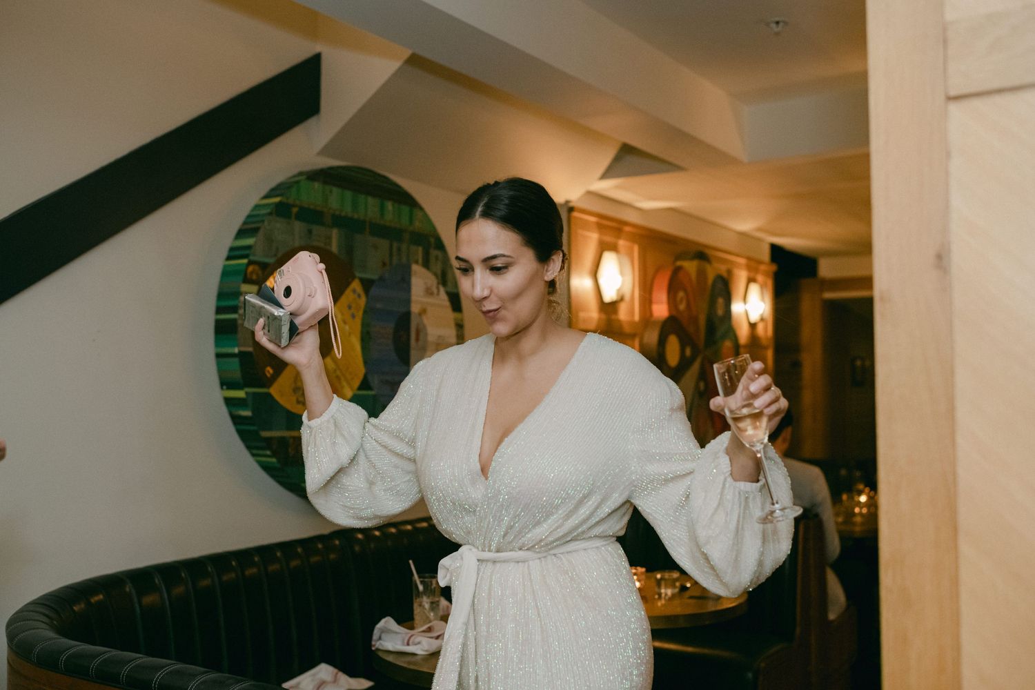 A woman in a white robe celebrating with raised champagne glasses in an elegant hallway.