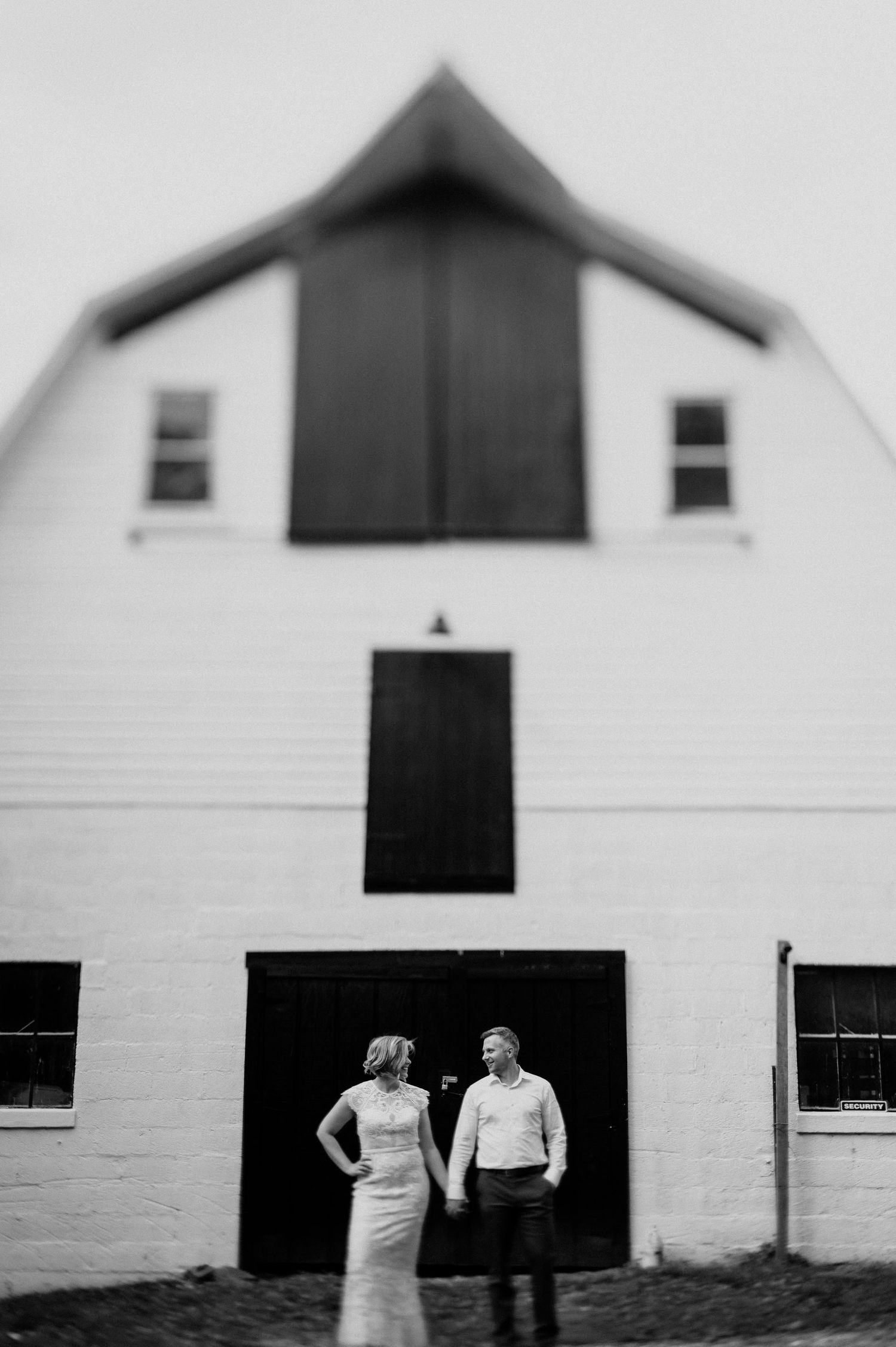 Minimalist black and white portrait against a white barn exterior.