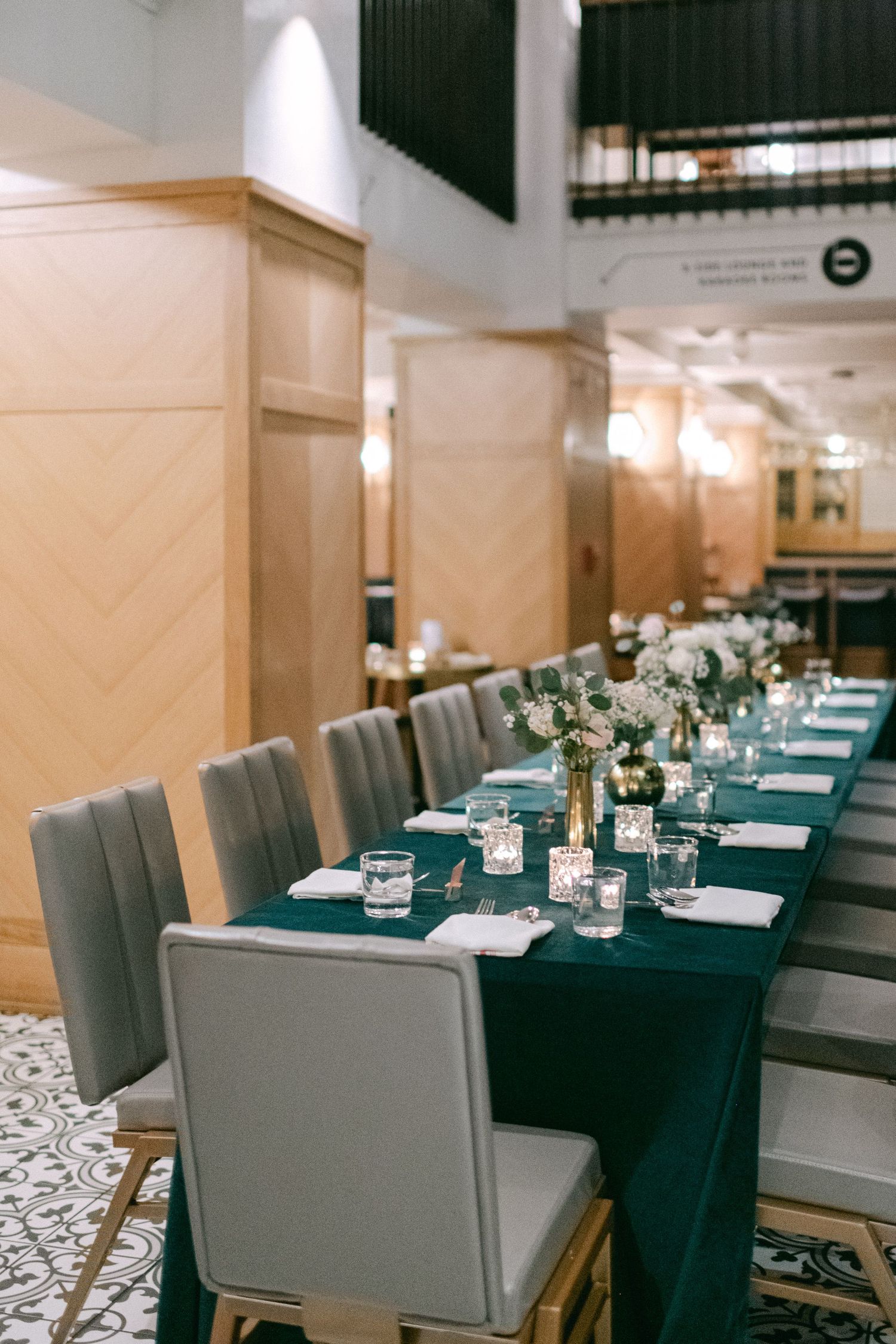 Long banquet table with emerald green linens and grey chairs set for a formal dinner.