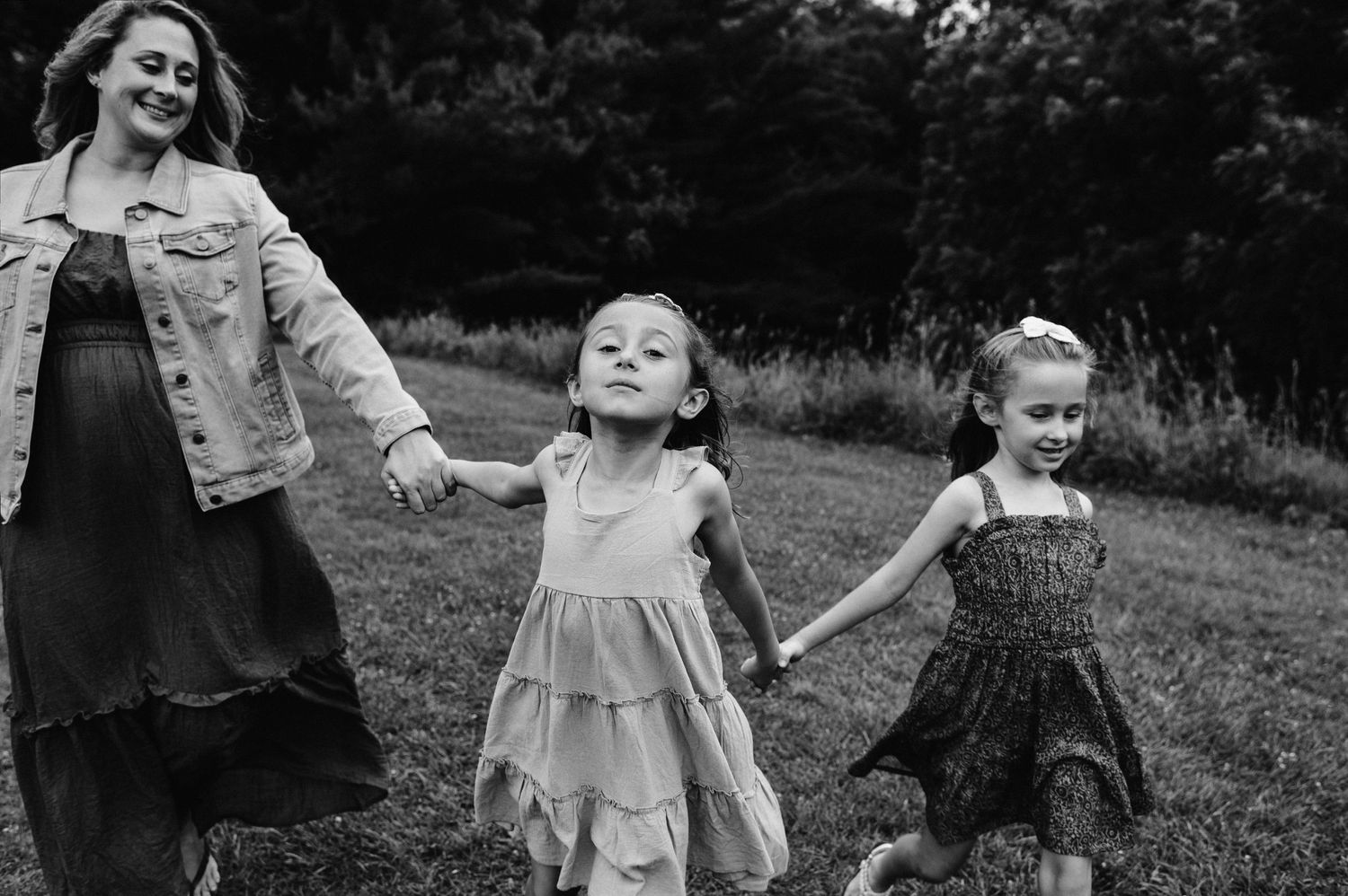 Black and white photo of family members dancing and holding hands while walking through a field.