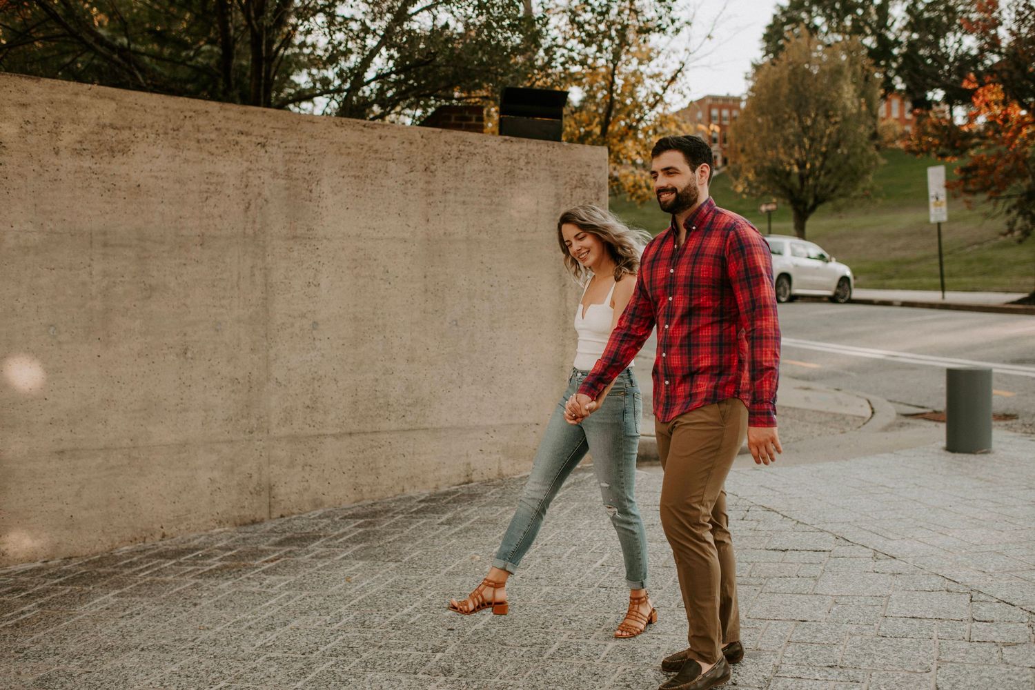 Playful couple walking together along concrete wall outdoors.