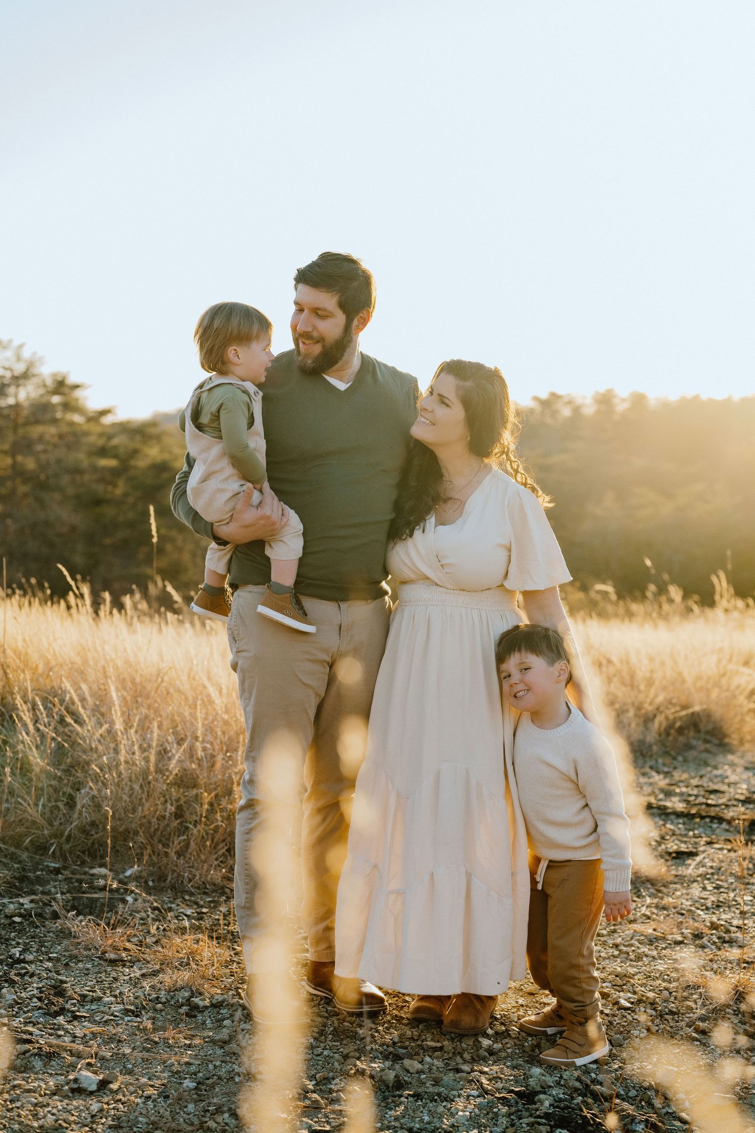 A family of four poses together in a golden field during sunset.