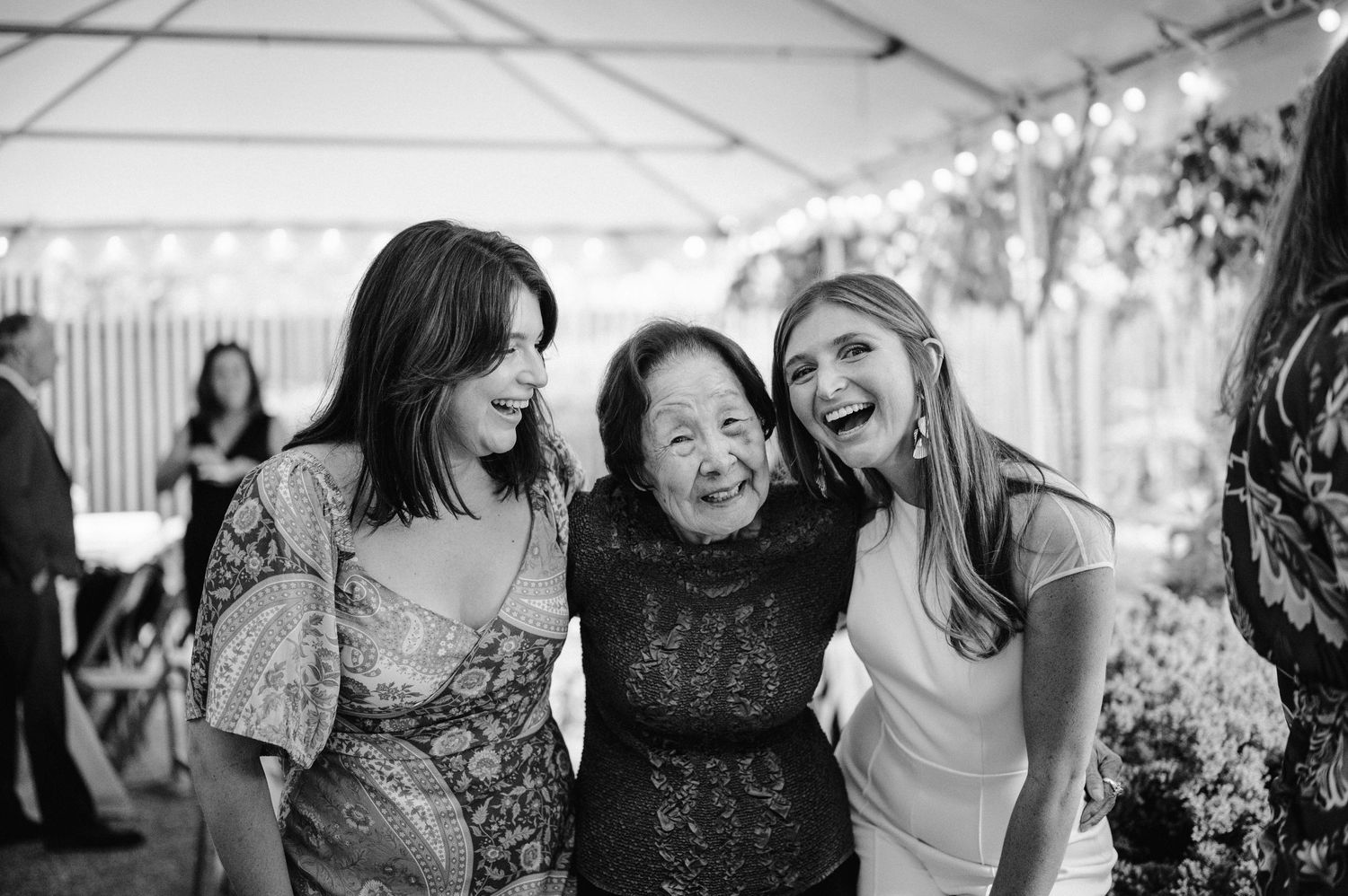 Three people sharing a joyful moment under a white tent at a celebration.