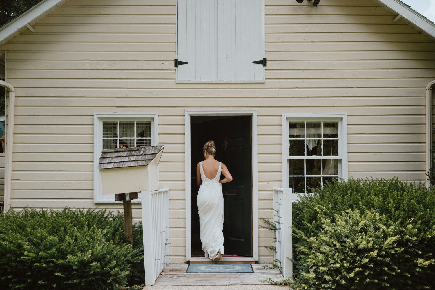 Classic white farmhouse exterior with bride entering through front doorway.