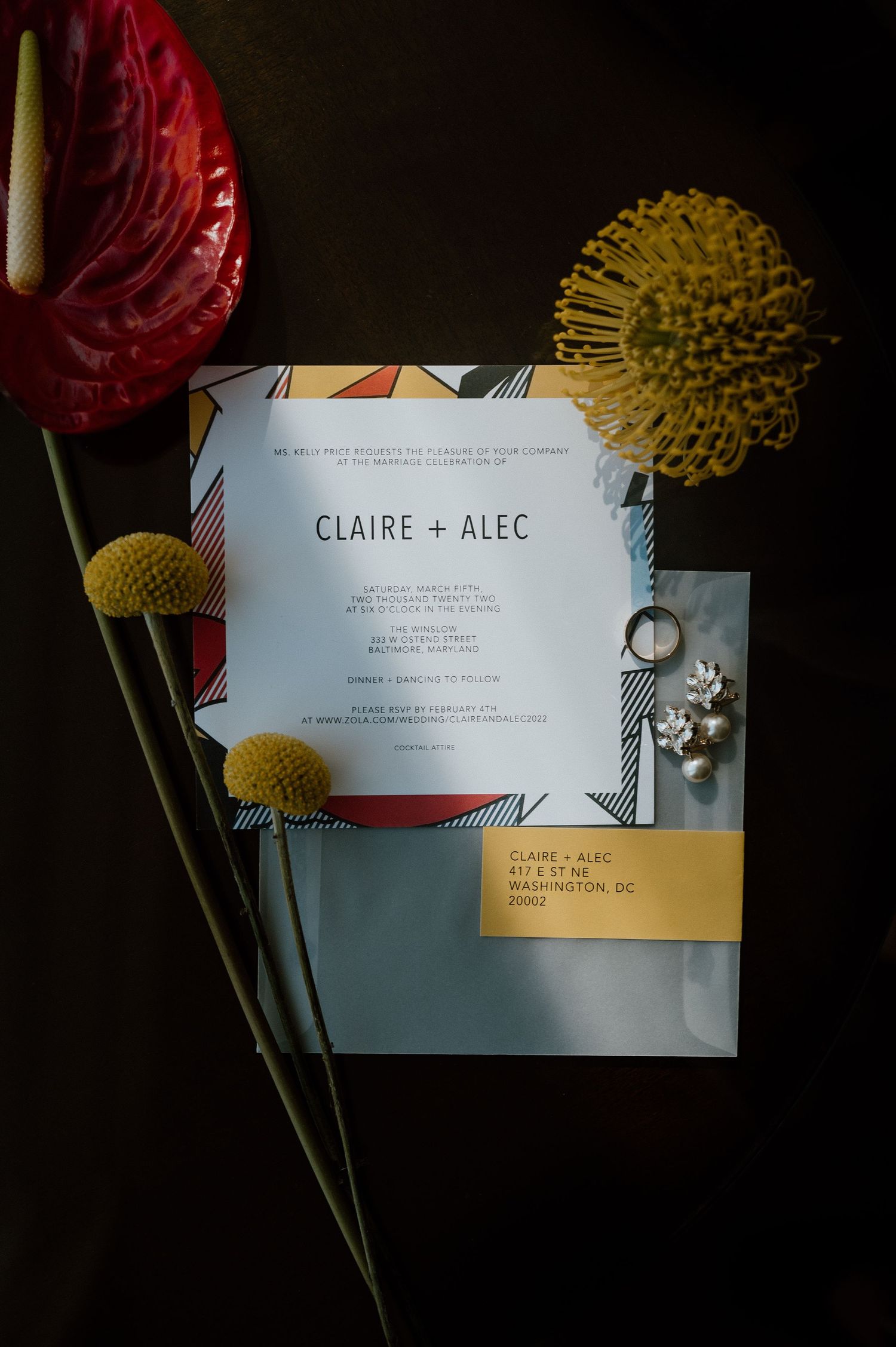 Wedding invitation for Claire and Alec displayed with red and yellow flowers and elegant jewelry details.