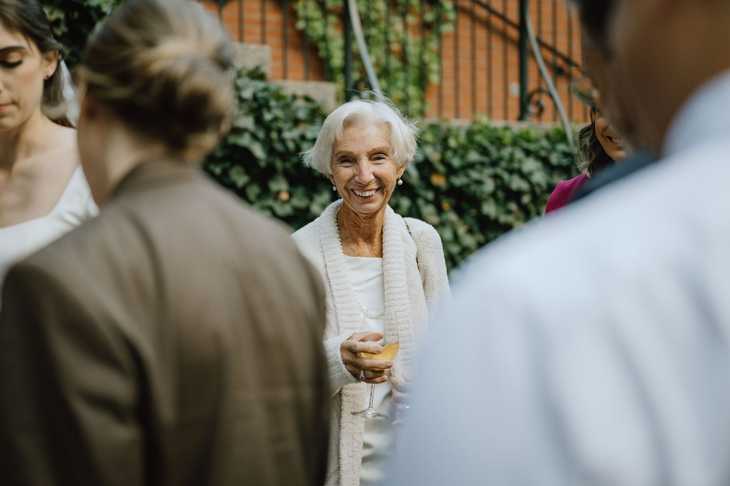 Guests enjoying drinks and conversation at an outdoor wedding reception with ivy-covered walls.