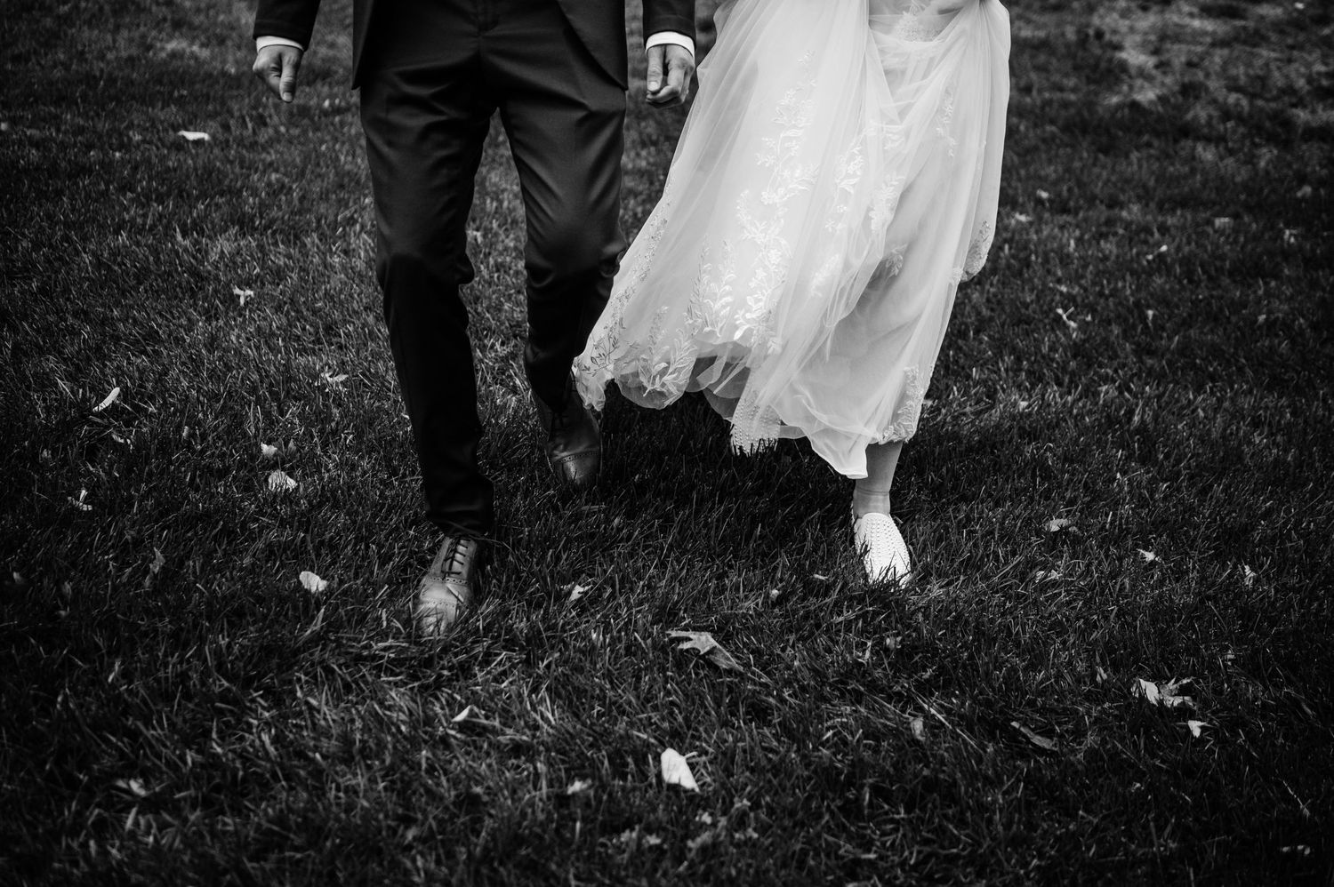 A black and white photo showing the lower half of a couple walking on grass.