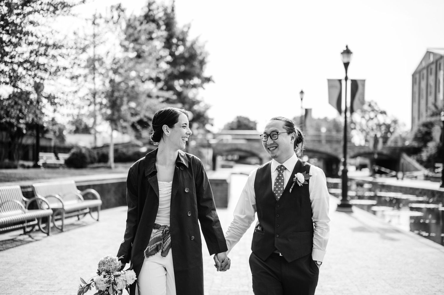 A couple walking hand in hand on a park path in black and white.