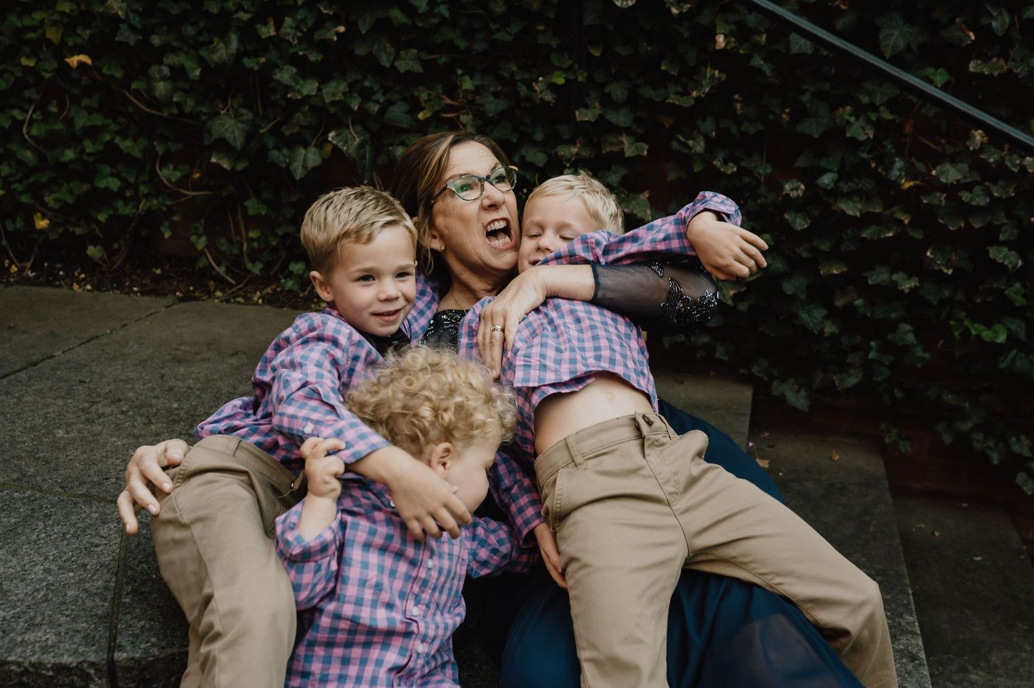A playful family moment captured in coordinated plaid shirts and khaki pants sitting outdoors.