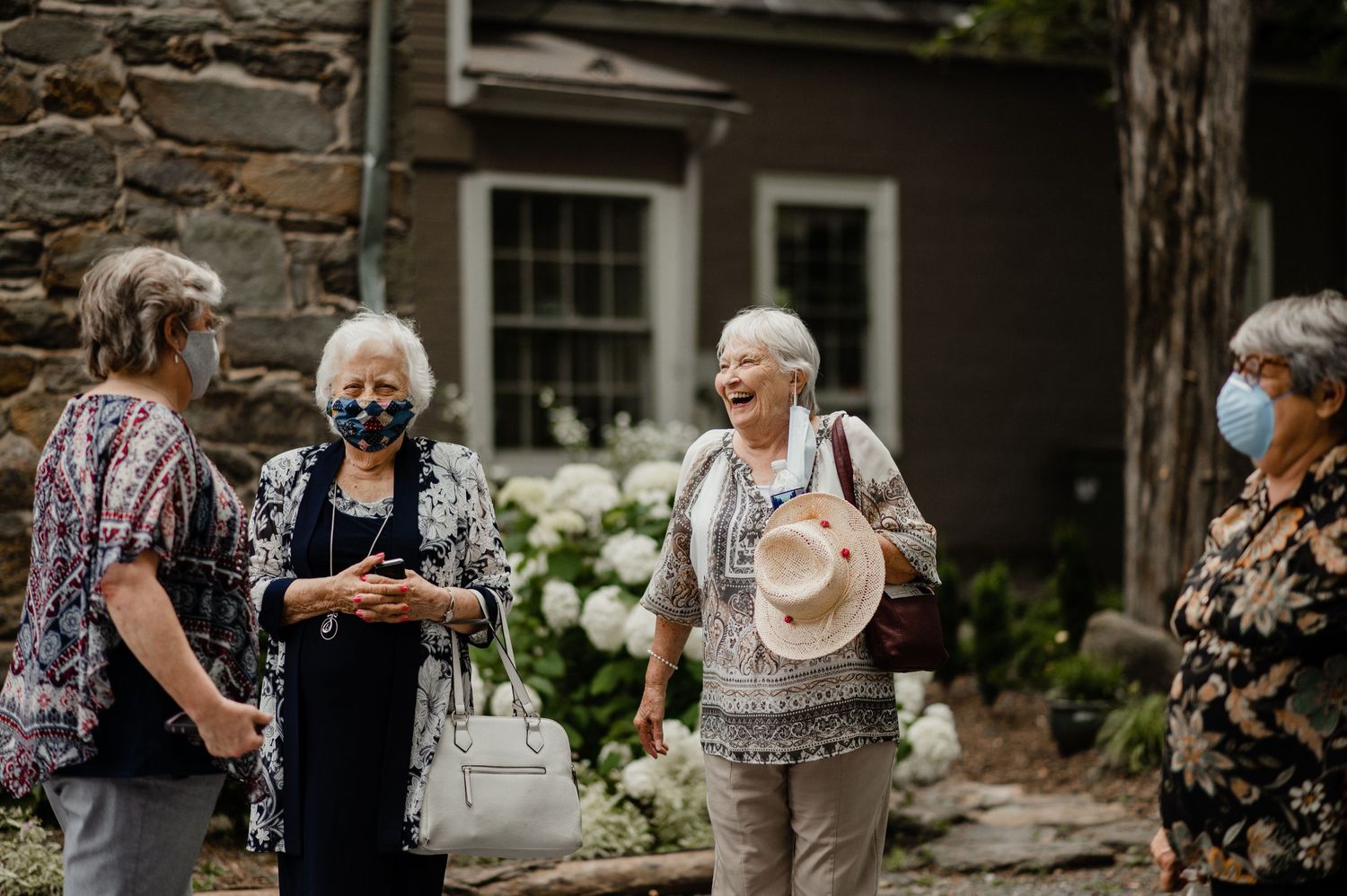 Group gathering outside a stone building with garden flowers and shrubbery.