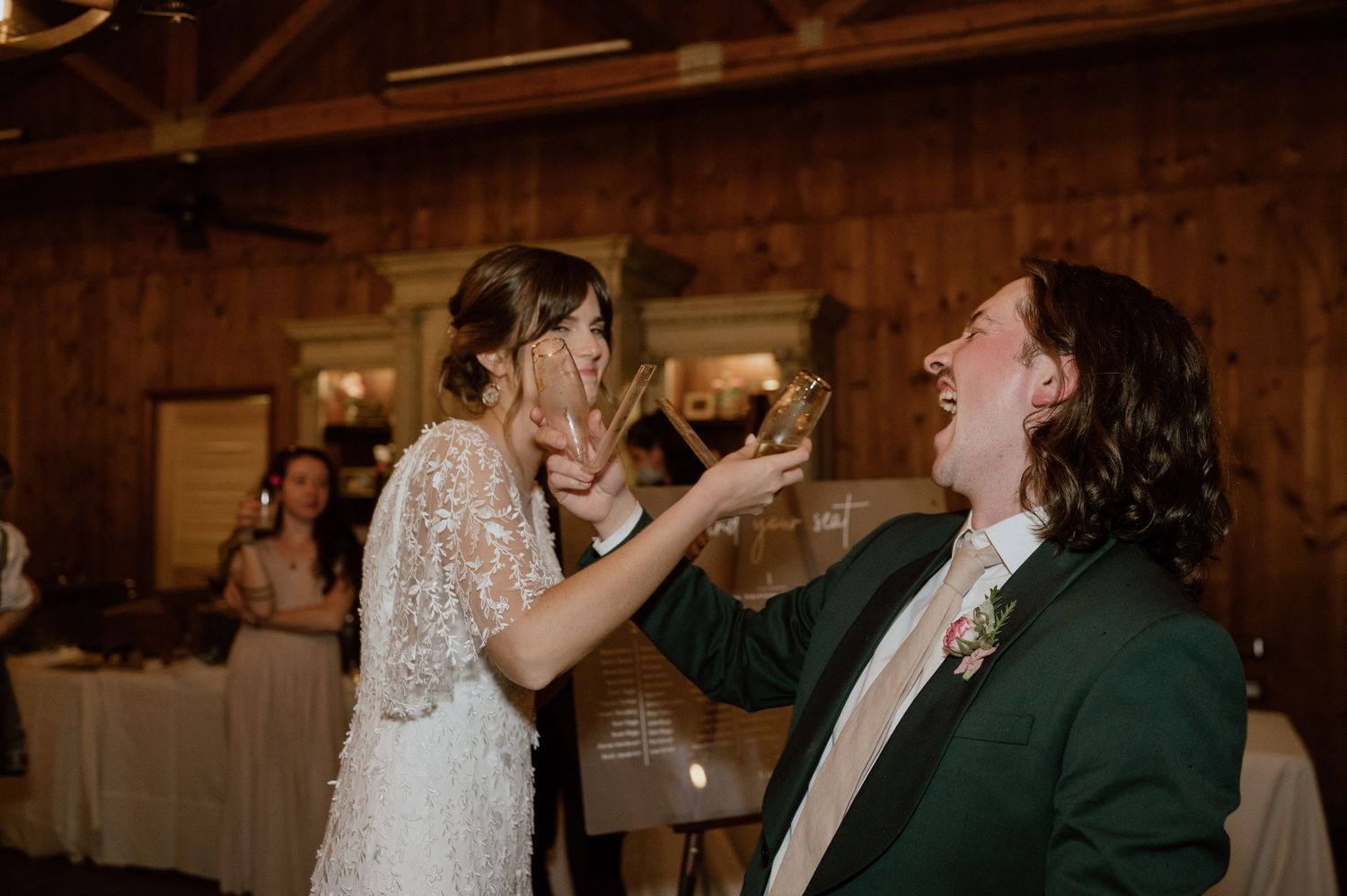 Playful couple feeding each other wedding cake at their reception in a wooden barn venue.