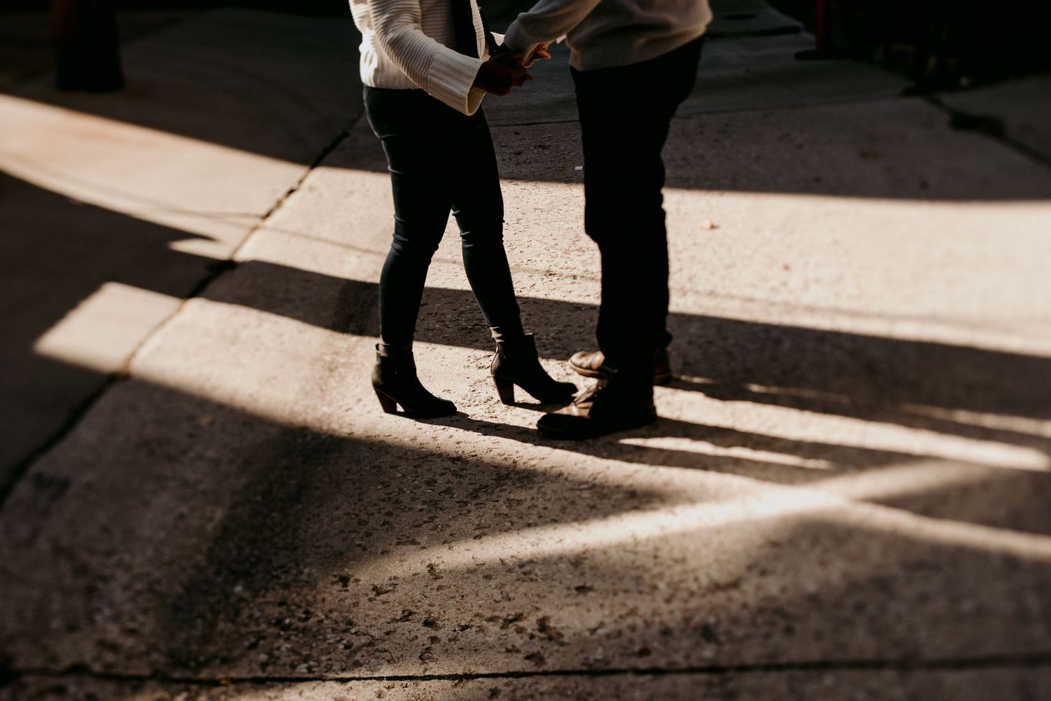 Two pairs of legs stand close together in dramatic sunlight and shadows.