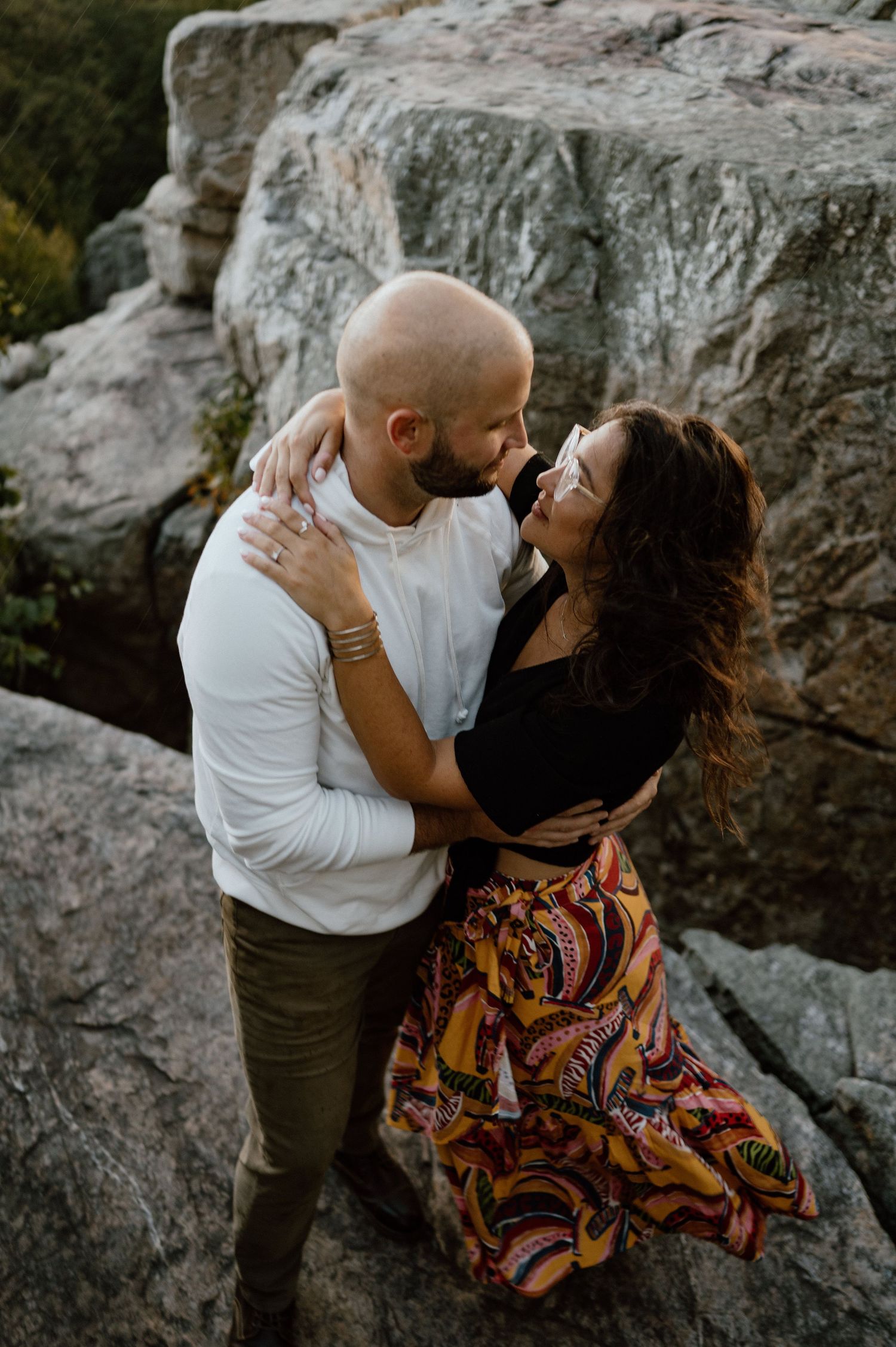 A couple shares an intimate moment on rocky mountain cliffs during sunset.