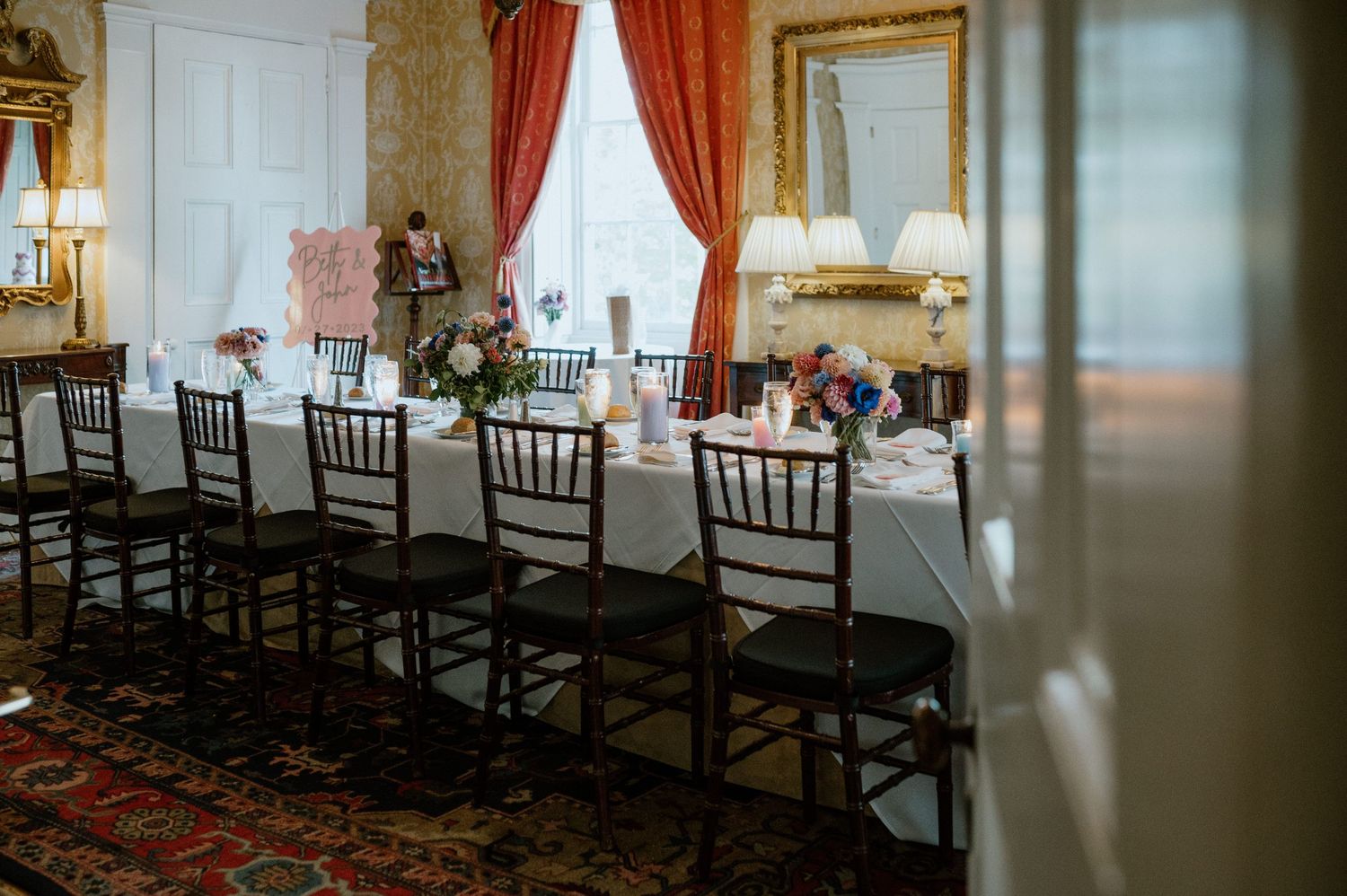 Elegant dining room setup with Chiavari chairs and white tablecloths in a historic mansion interior.