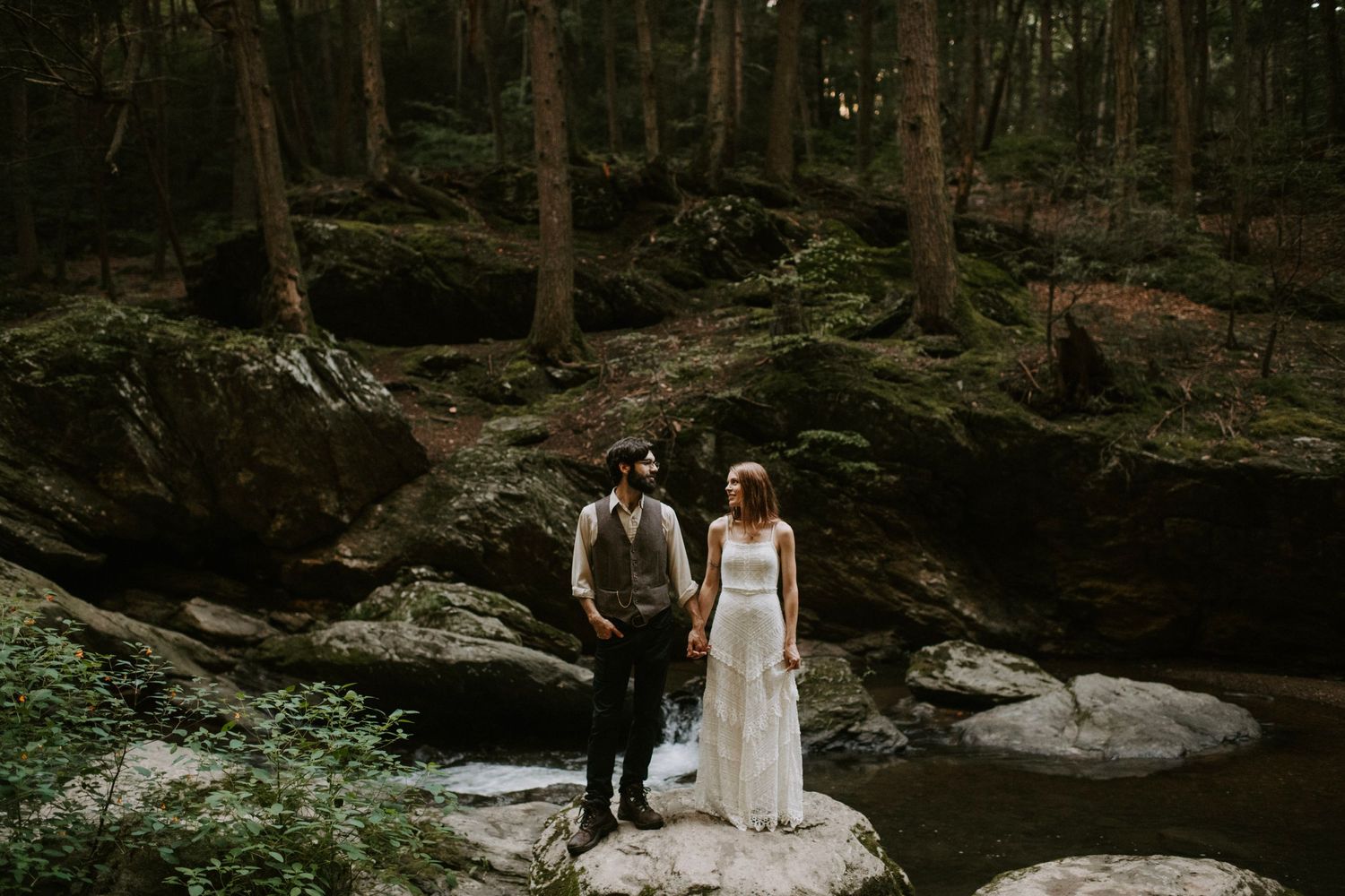 Couple stands on large rocks in a dramatic forest landscape.