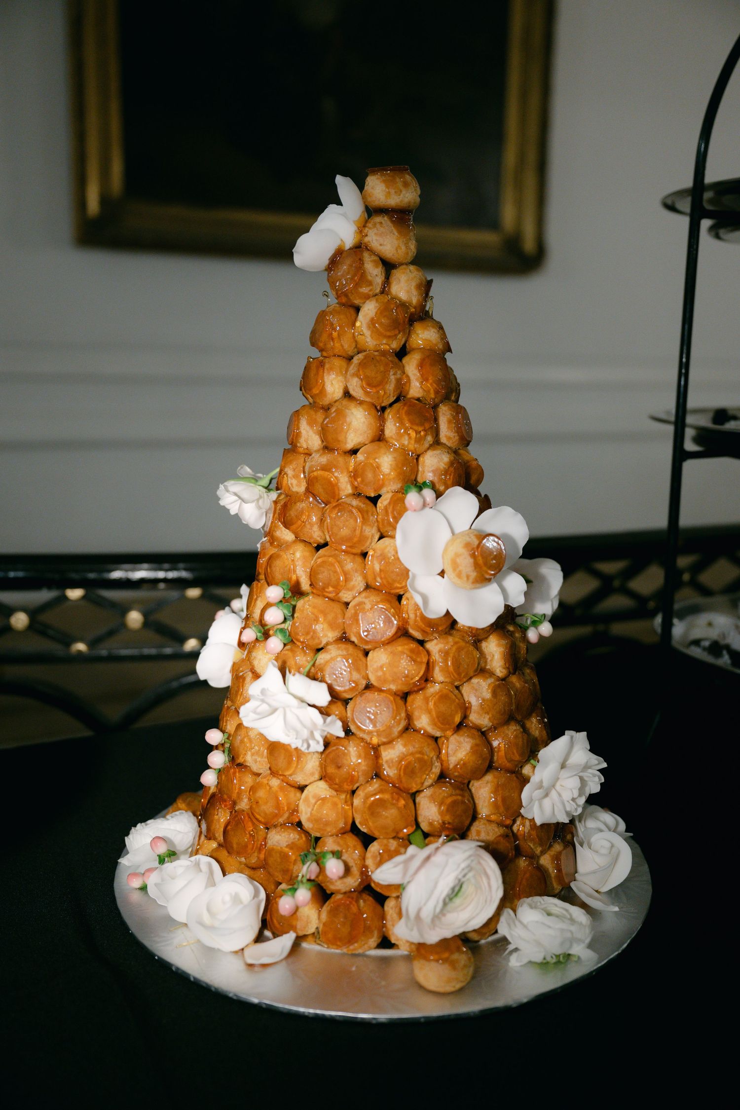 Progressive shots showing the assembly stages of a croquembouche dessert tower decorated with white cream and caramel drizzle.